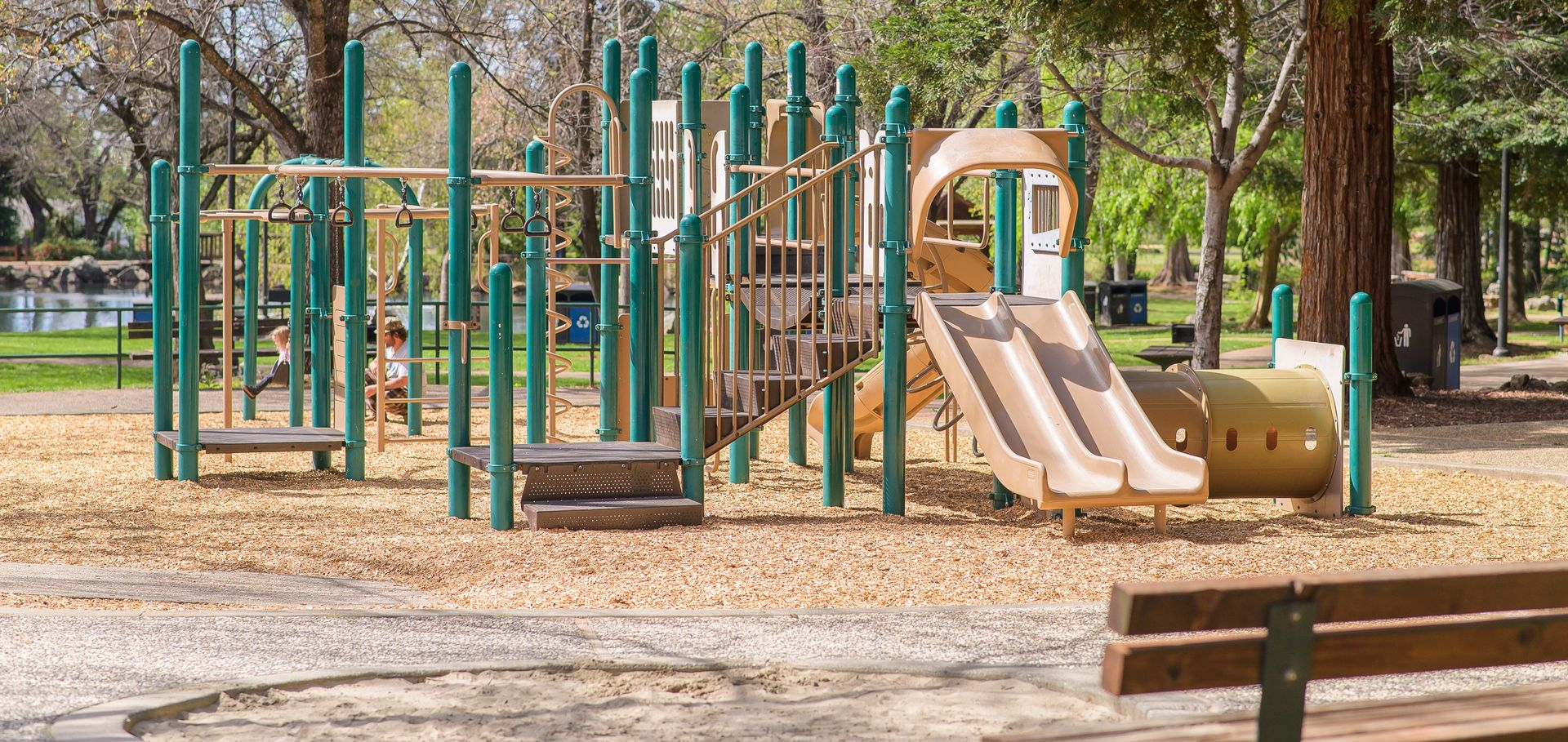 Empty playground with green climbing structures and tan slides in a park