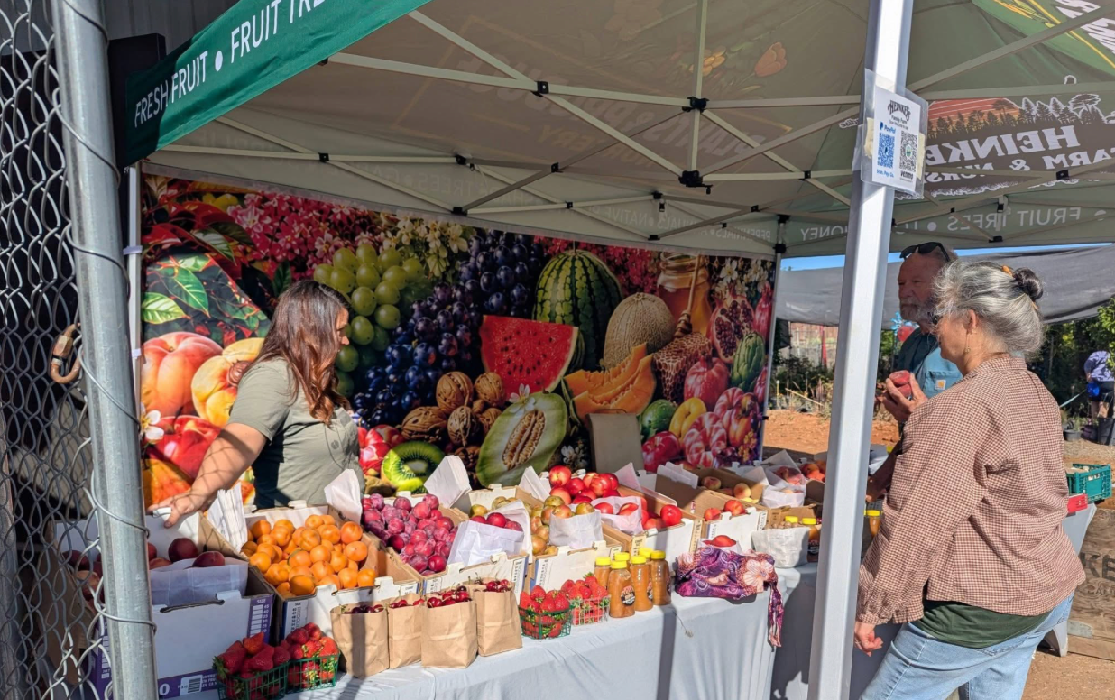 Outdoor fruit stand with colorful produce and two shoppers under a canopy