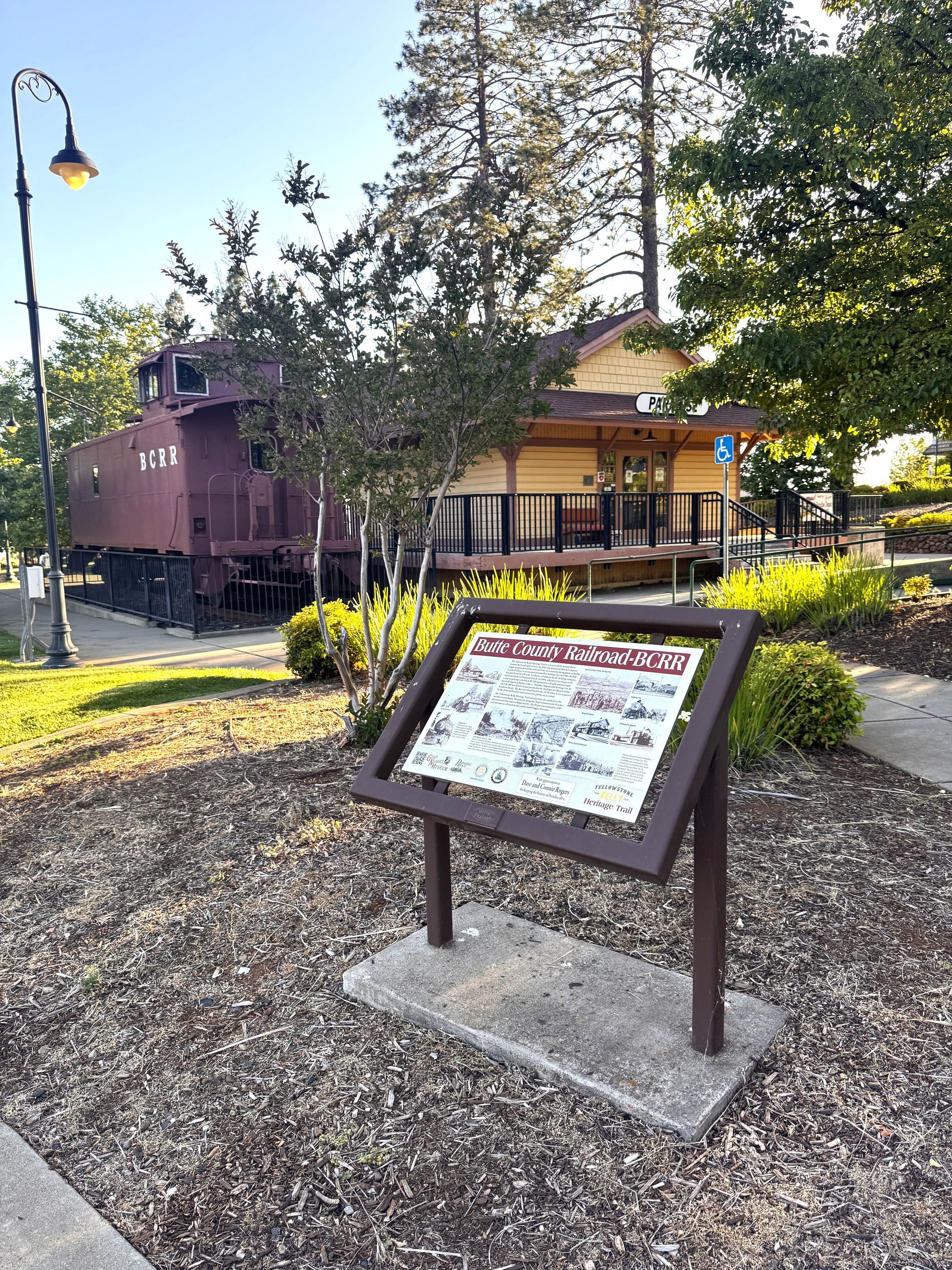 A sign in front of a train car in a park.
