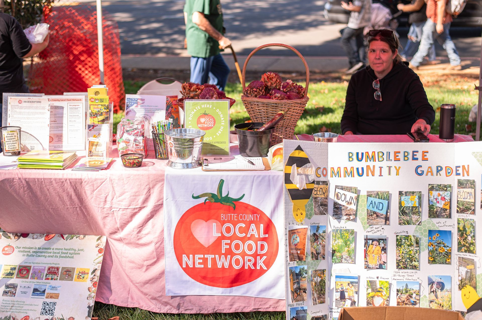 Local food network and community garden booth at an outdoor market, with produce displays and informational posters.