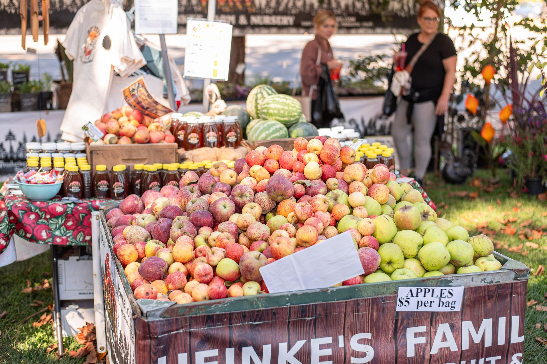 Farm stand with baskets of colorful apples and pears, with people browsing in the background.