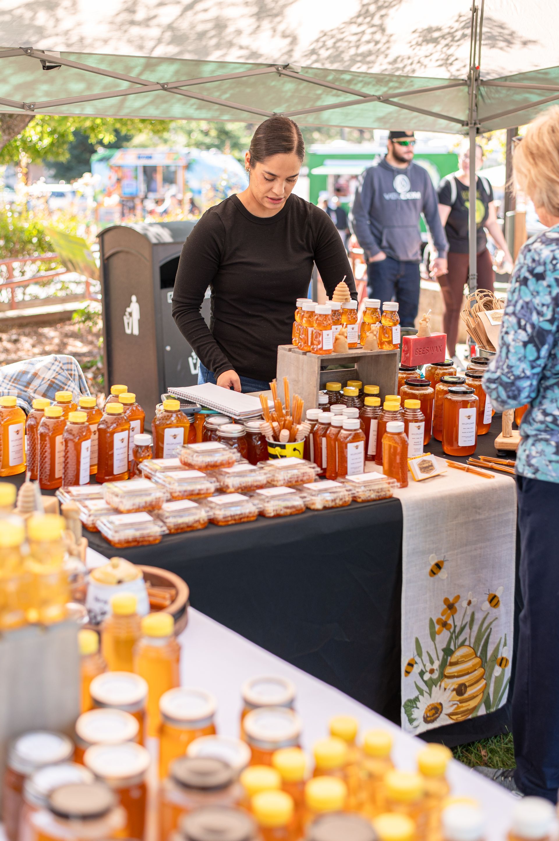 Outdoor market stall with jars of honey and preserves on a table under a canopy