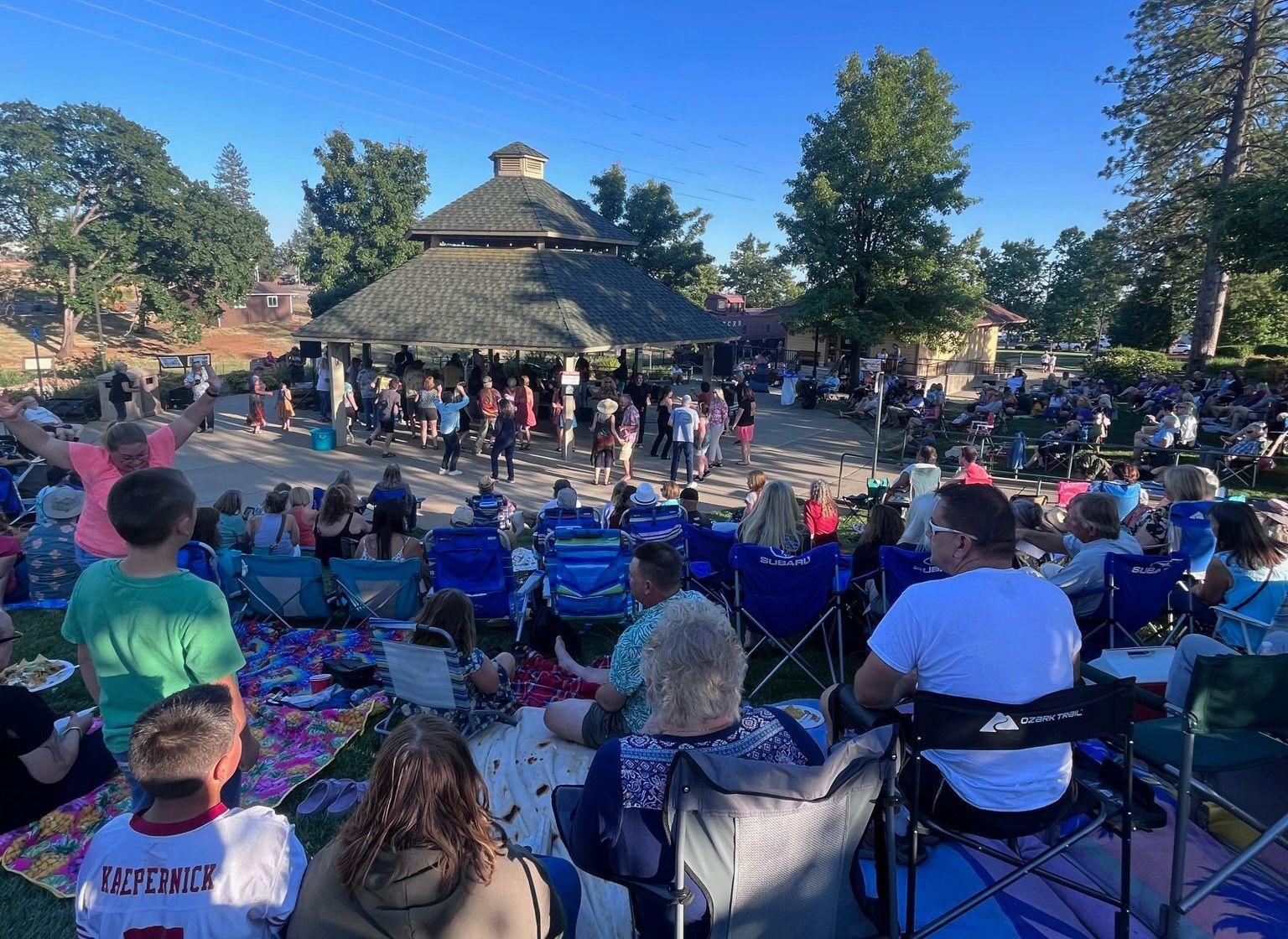 A group of people are sitting in chairs in a park watching a concert in Paradise and Magalia, California