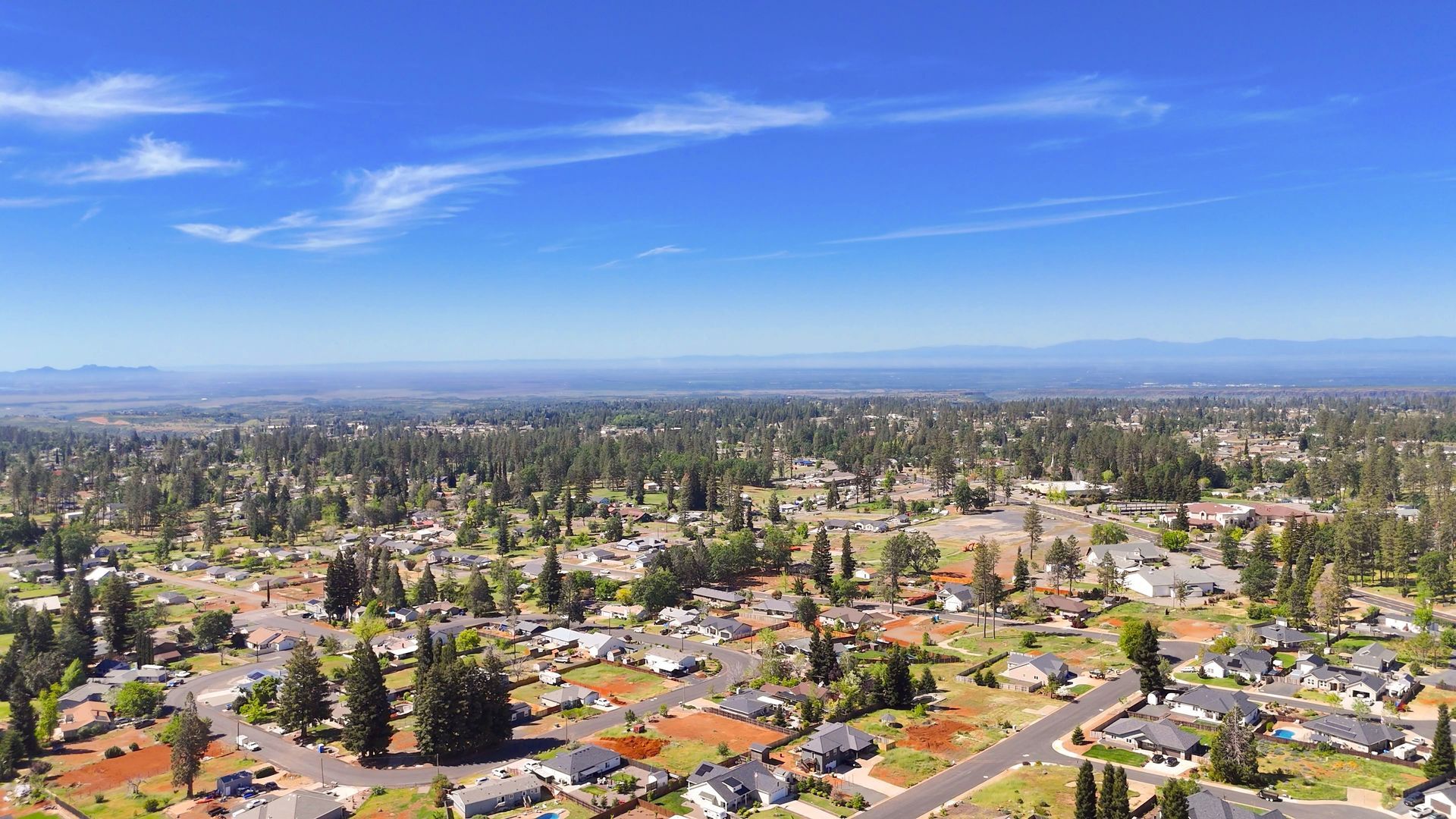 Aerial view of a suburban neighborhood with houses, trees, and a clear blue sky.