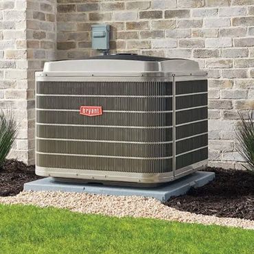 Outdoor air conditioner unit beside a brick house wall and green lawn