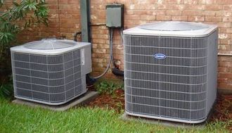 Two outdoor air conditioner units beside a house on a grassy lawn.