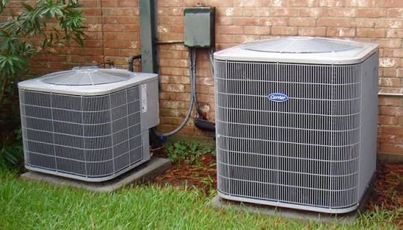 Two outdoor air conditioner units beside a house on a grassy lawn.