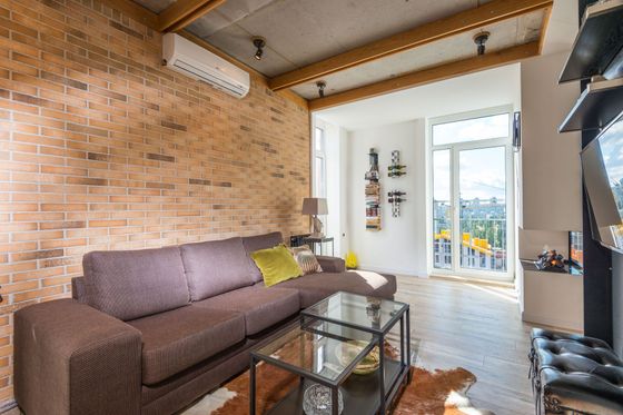 Loft living room with exposed brick wall, brown sofa, glass coffee table, and balcony doors.