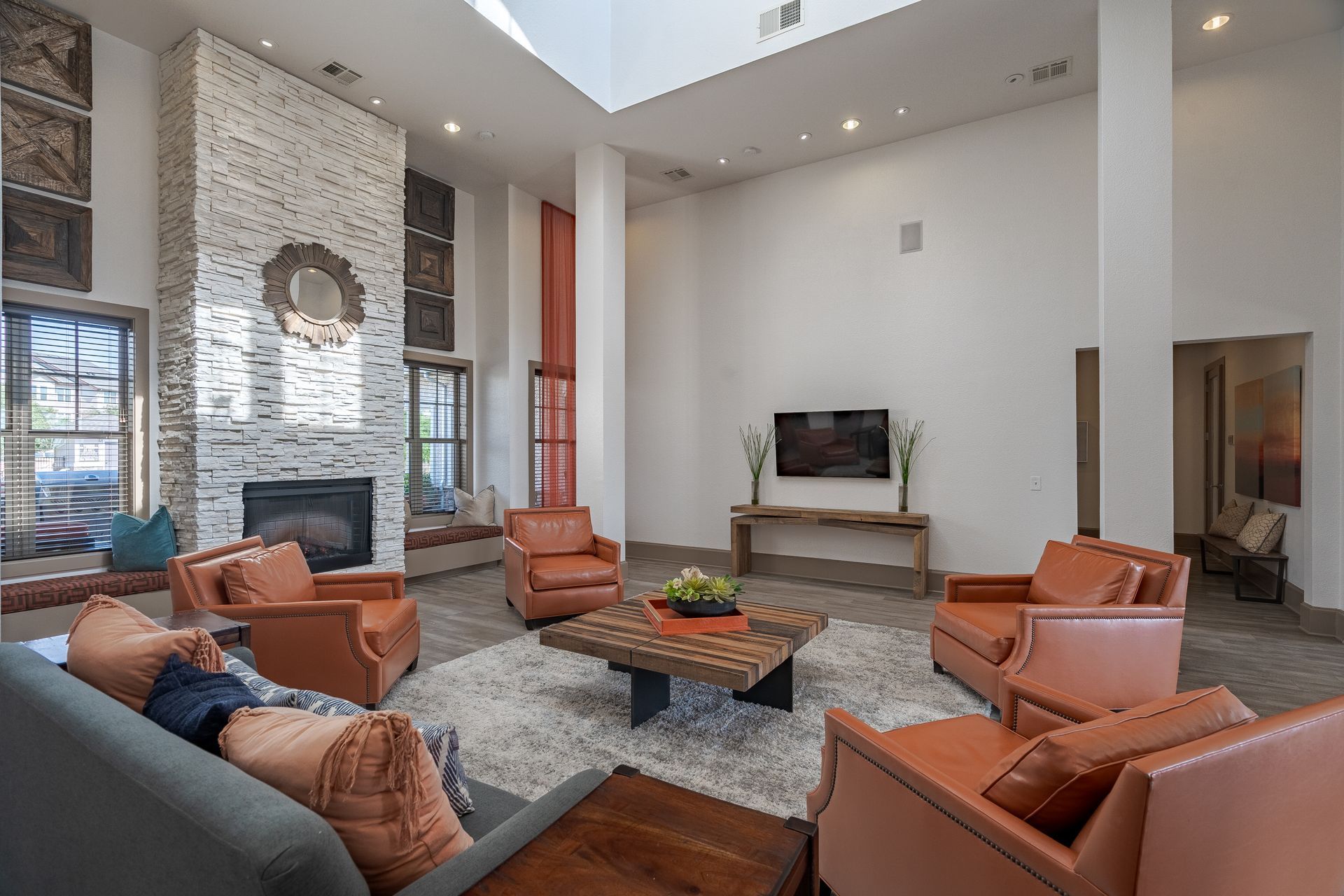 Communal lounge with a stone fireplace, orange leather chairs, and a wall-mounted TV at Tradewinds Apartments, offering apartments for rent in Midland, TX near I-20.