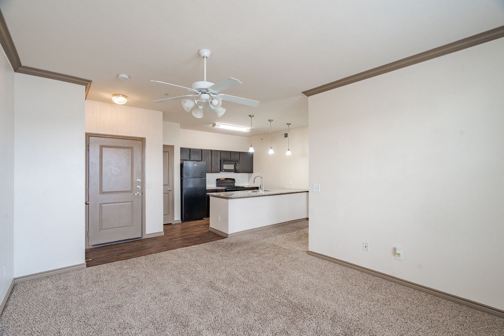 Open-concept living area with kitchen island, black appliances, and ceiling fan at Tradewinds Apartments, offering apartments in Midland, TX.