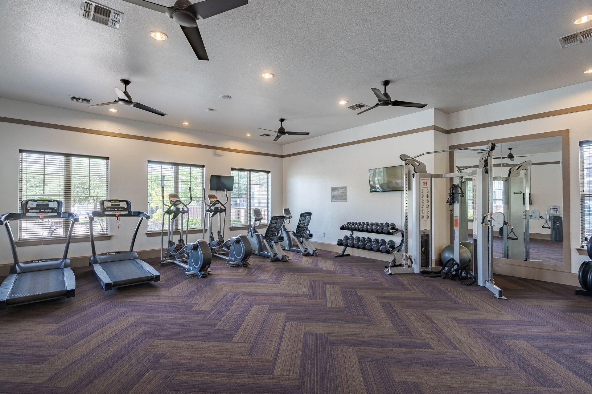 Interior view of a community gym with treadmills, ellipticals, and weight machines at Tradewinds Apartments, offering apartments for rent in Midland, TX.
