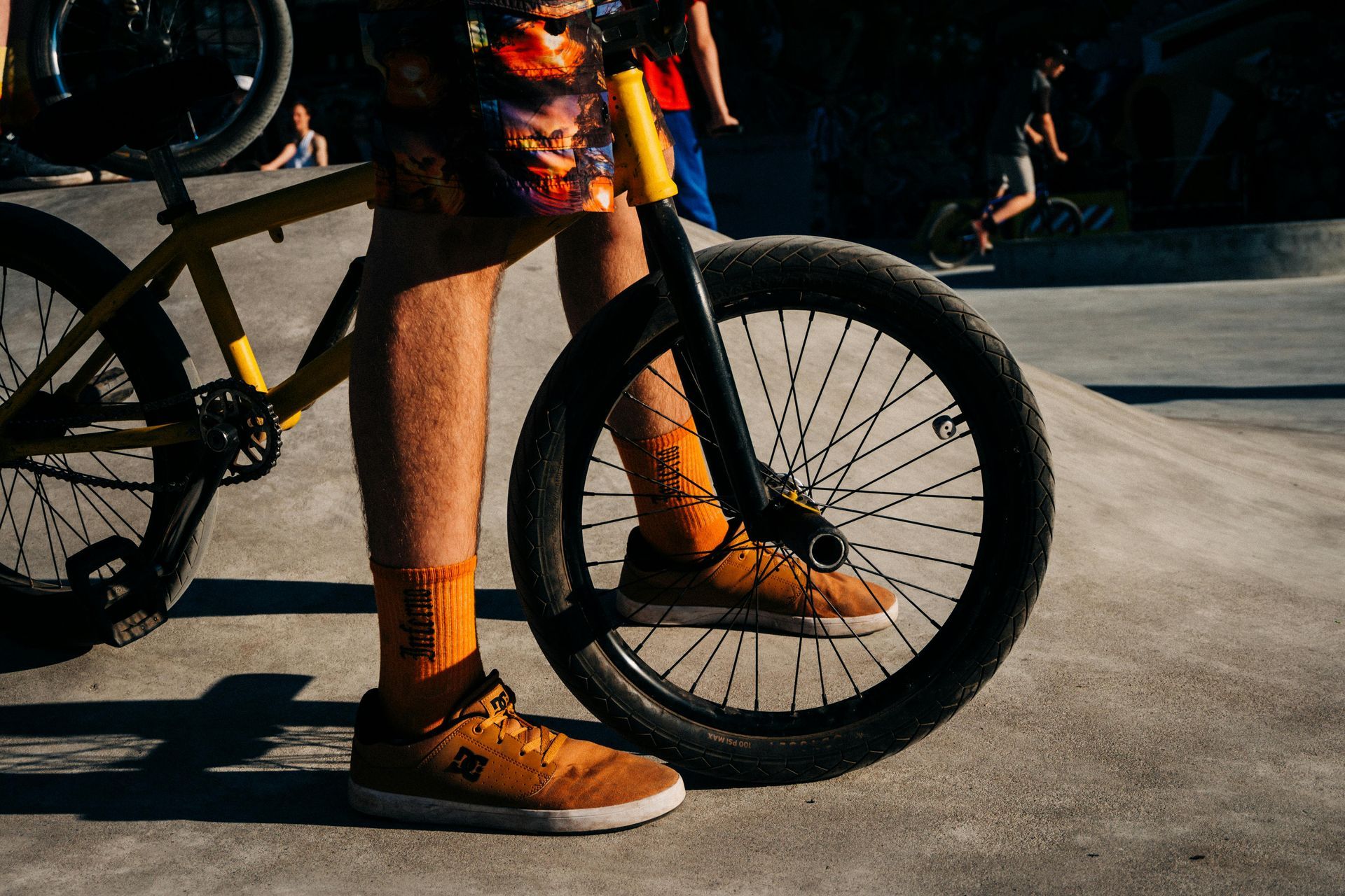 Person standing beside a mountain bike, wearing orange socks and shoes on a concrete surface.