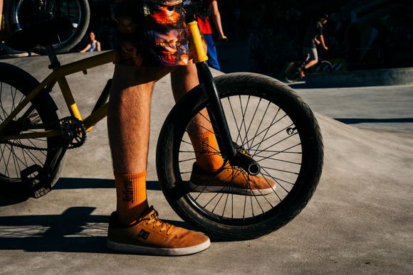 Person standing beside a mountain bike, wearing orange socks and shoes on a concrete surface.