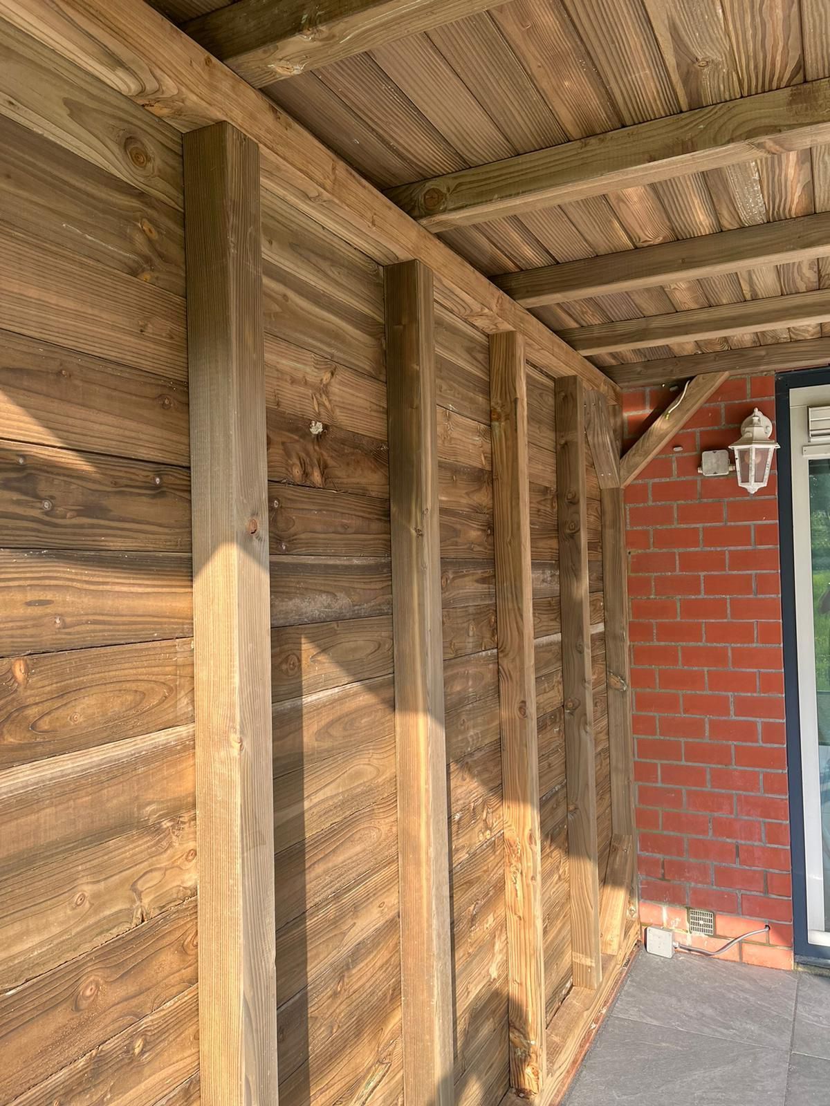 Buitenkant van het houten gebouw met verticale balken, gevelbekleding met structuur en een bakstenen muur.
