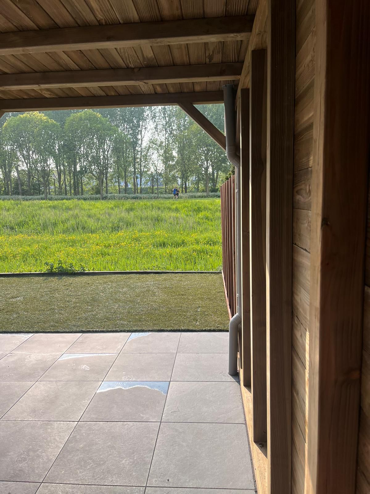Uitzicht vanaf een houten schuilplaats, met zicht op een grasveld met bomen.