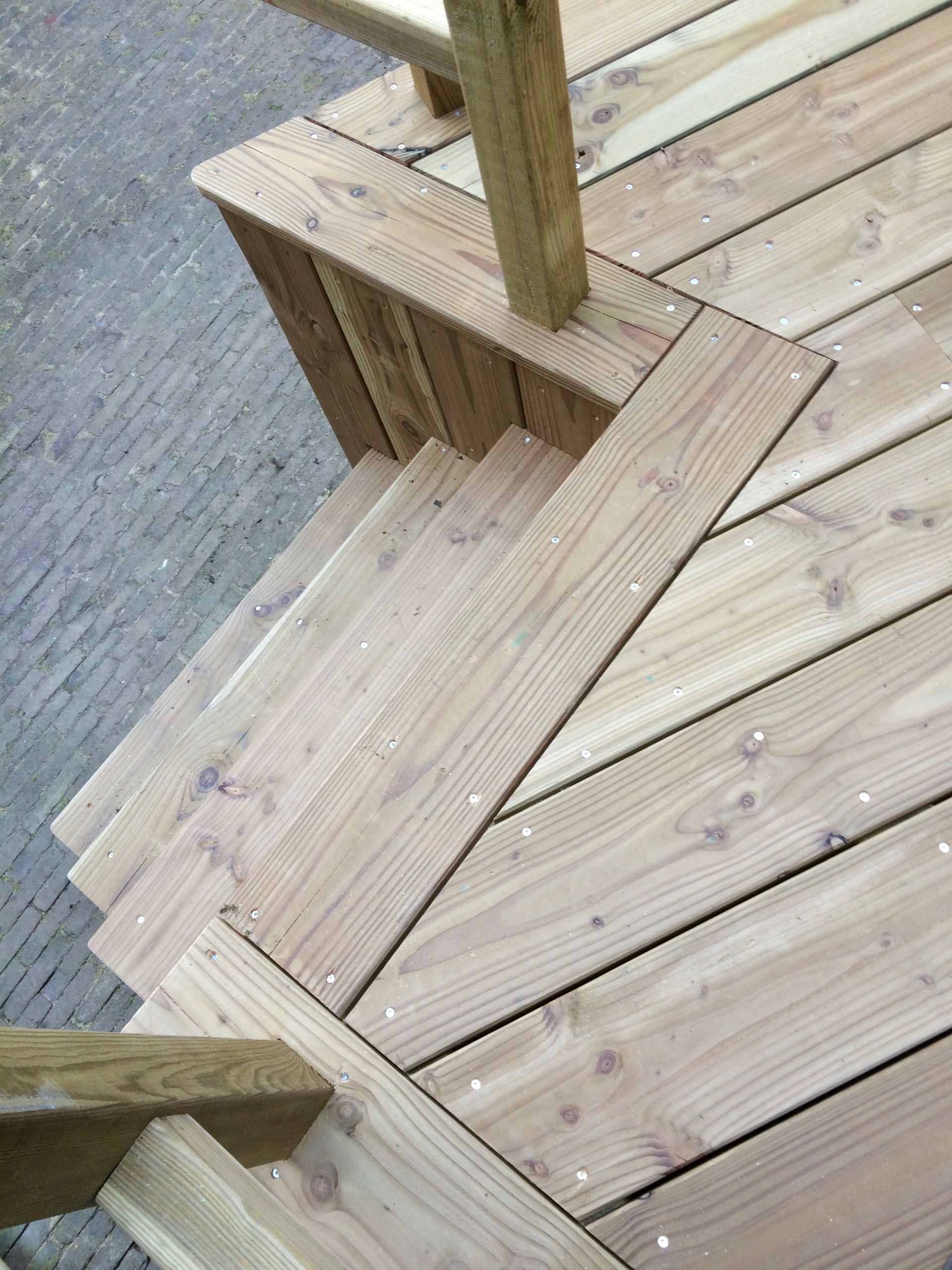 Houten terras met een schuin aflopende trap. Planken en palen zijn zichtbaar.