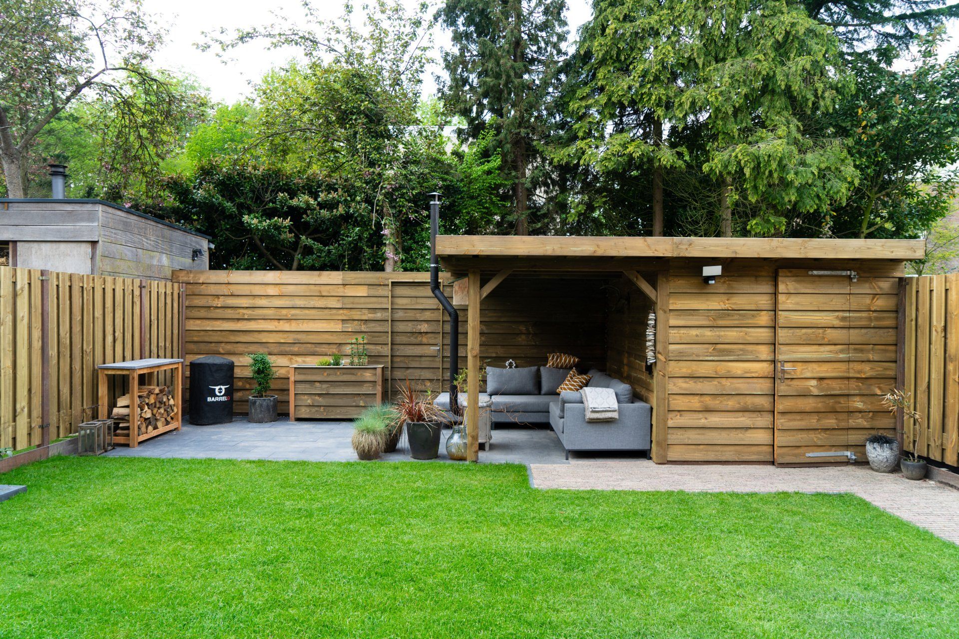 Houten terras in de achtertuin met zitgedeelte, opbergruimte en een weelderig groen gazon.