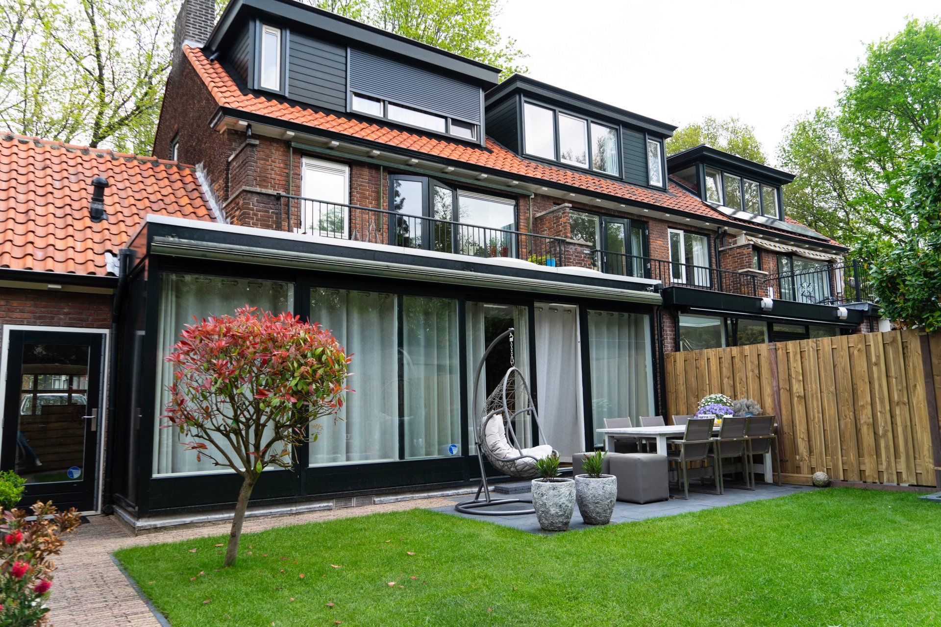 Bakstenen huis met groen gazon, zitgedeelte buiten en een rode boom.
