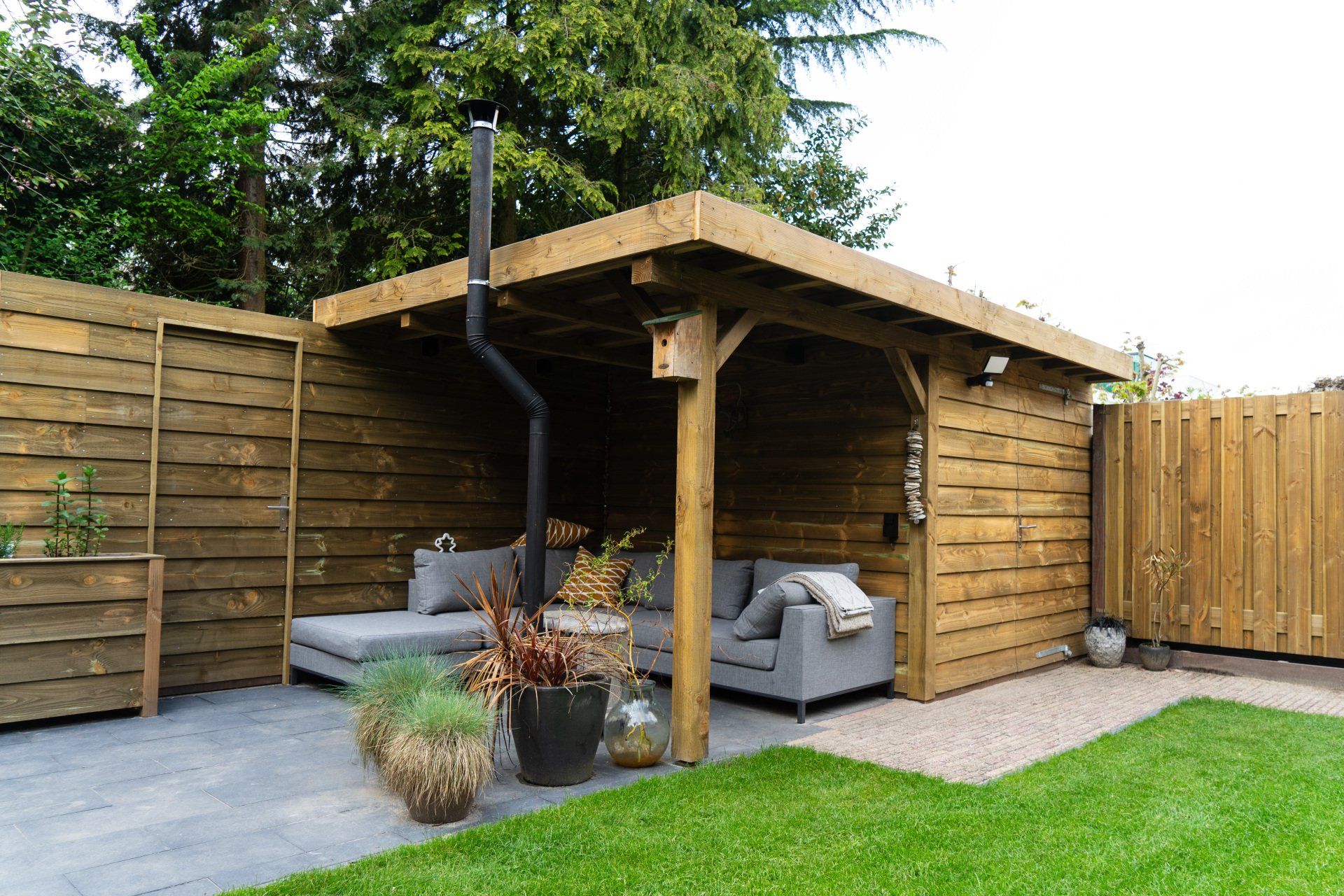 Houten buitenruimte met bank, planten en een klein grindpad.