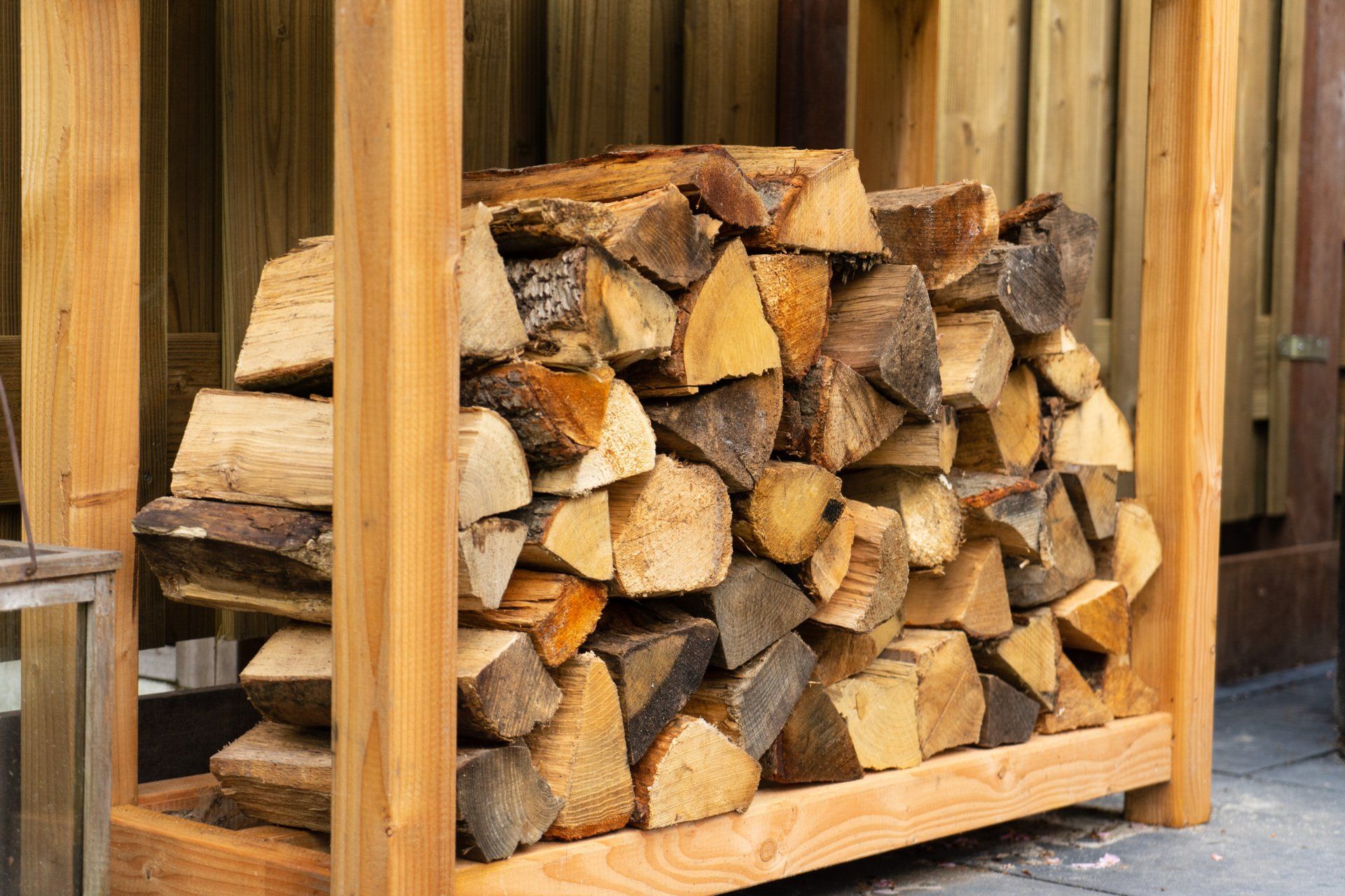 Houtstapel in een houten rek; diverse kleuren hout netjes opgestapeld in de buitenlucht.