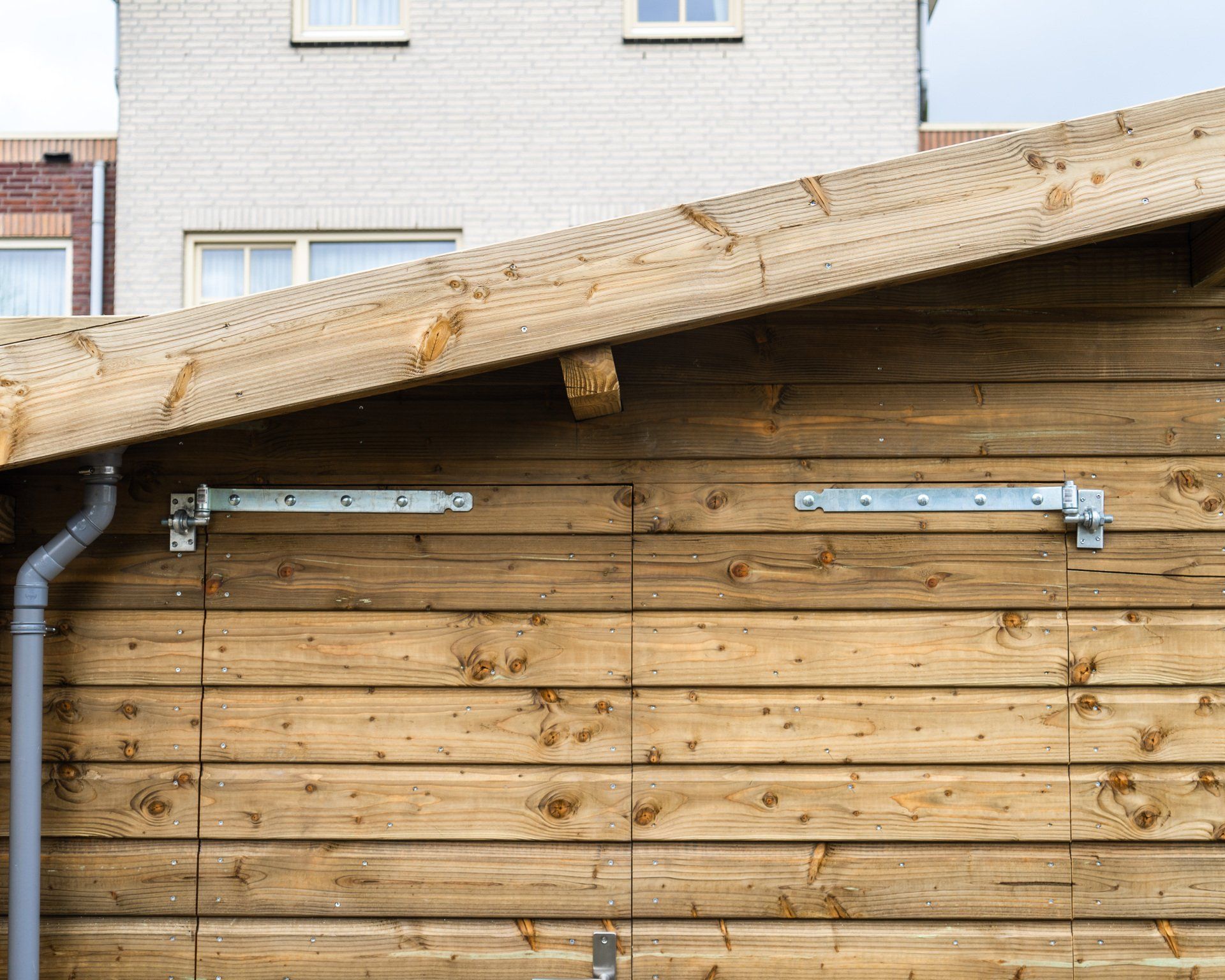 Houten schuur met metalen scharnieren en een regengoot tegen een bakstenen gebouw.