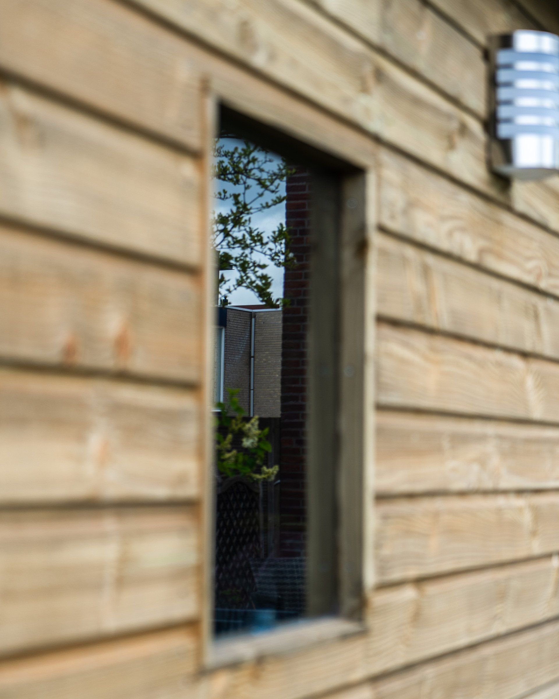 Een raam dat het buitenlandschap weerspiegelt, is ingebouwd in een houten muur.