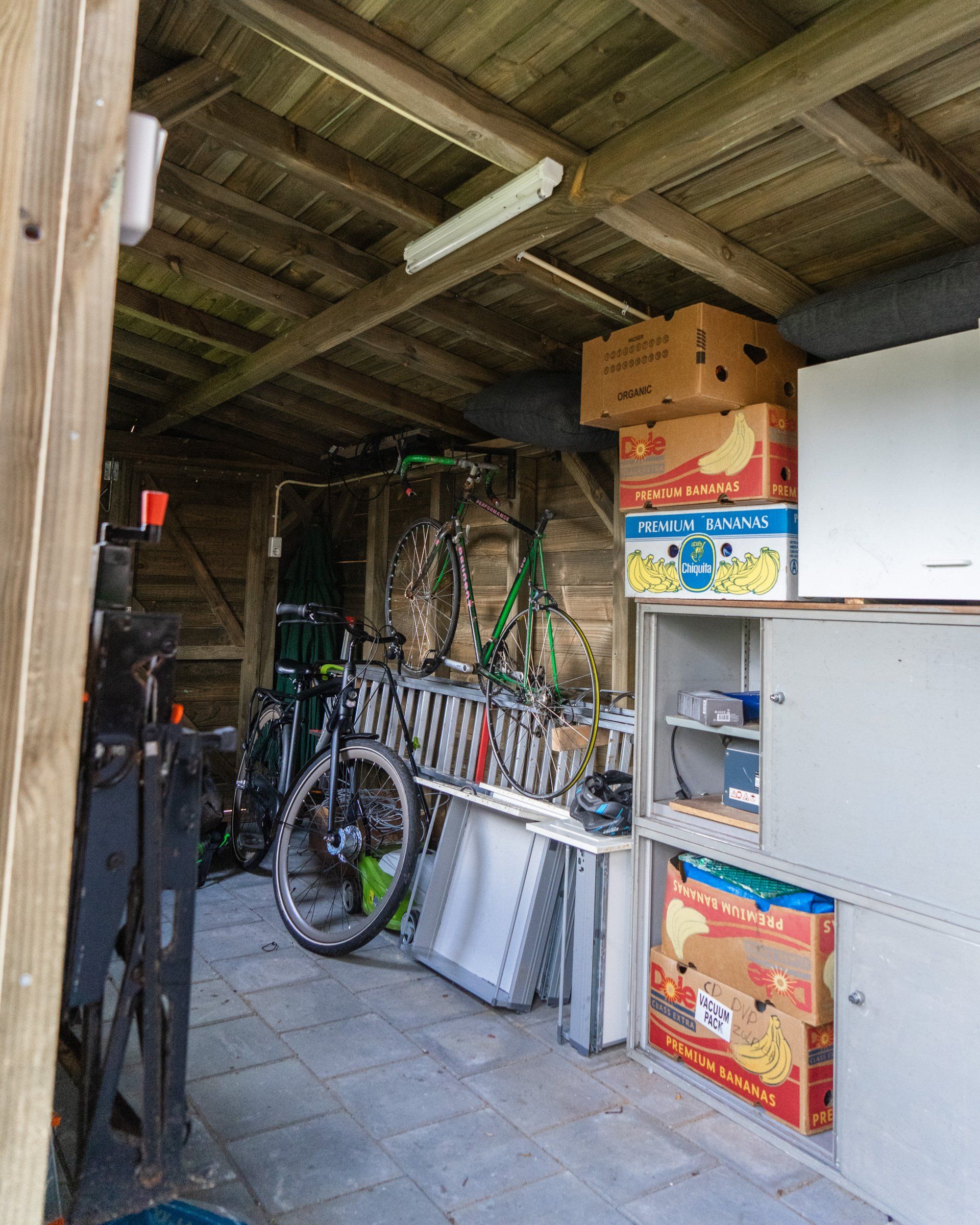 Interieur van een rommelige schuur. Fietsen, dozen en een metalen kast staan ​​erin opgeslagen.