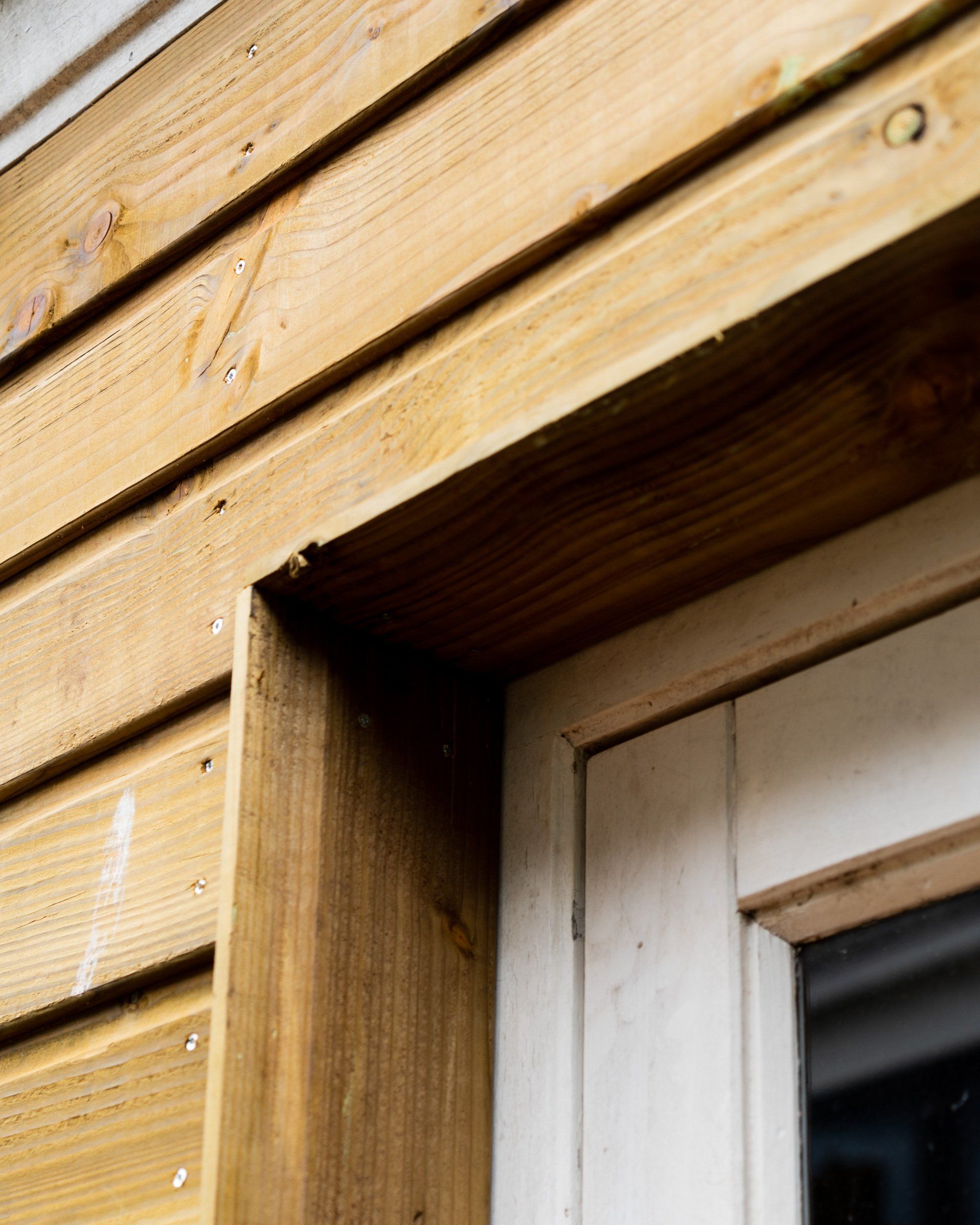 Detailopname van houten gevelbekleding en raamkozijn, met verweerd hout en witte sierlijsten.