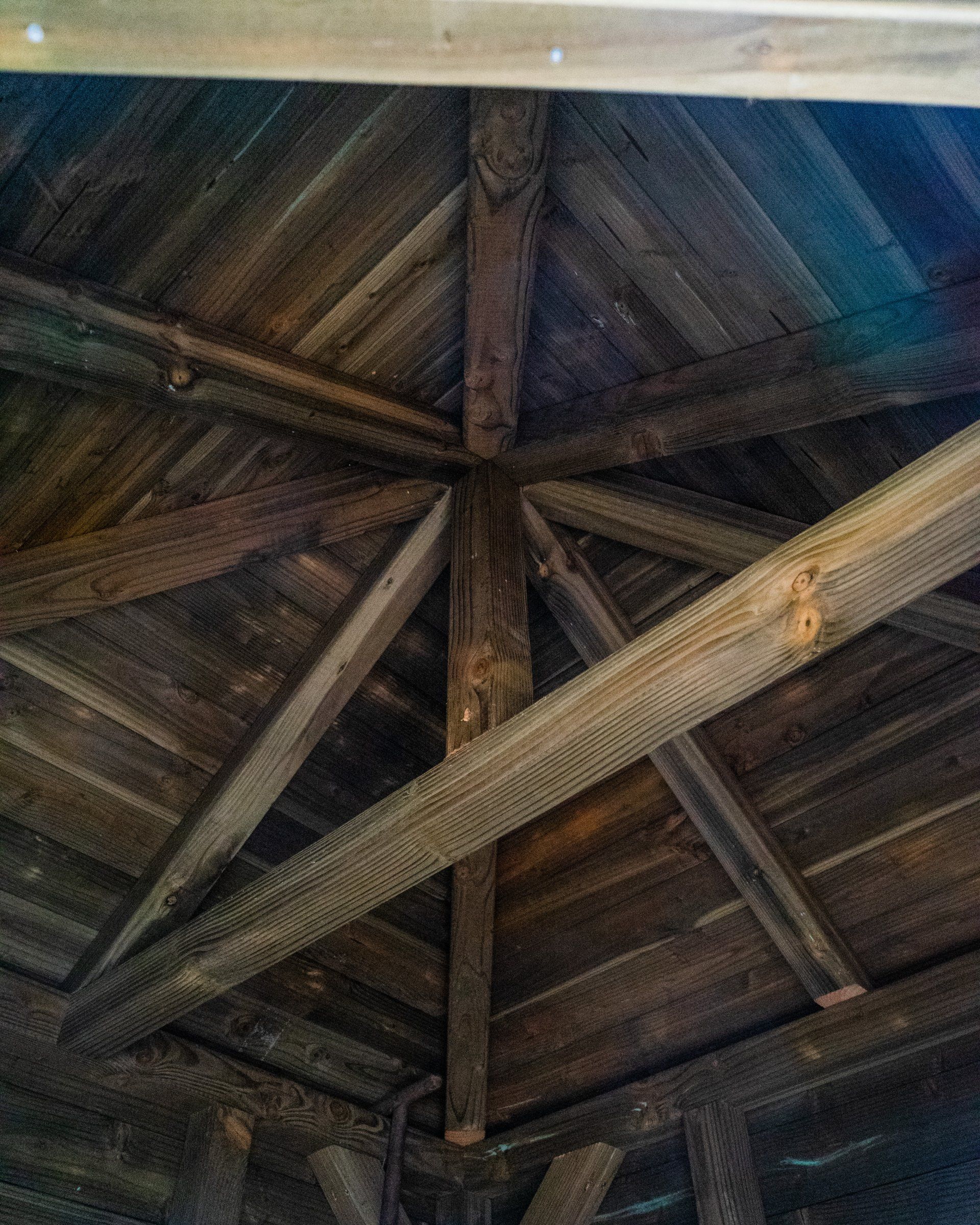 Houten dakconstructie voor een tuinpaviljoen, met schuin geplaatste balken die samenkomen bij een centrale steunpaal.