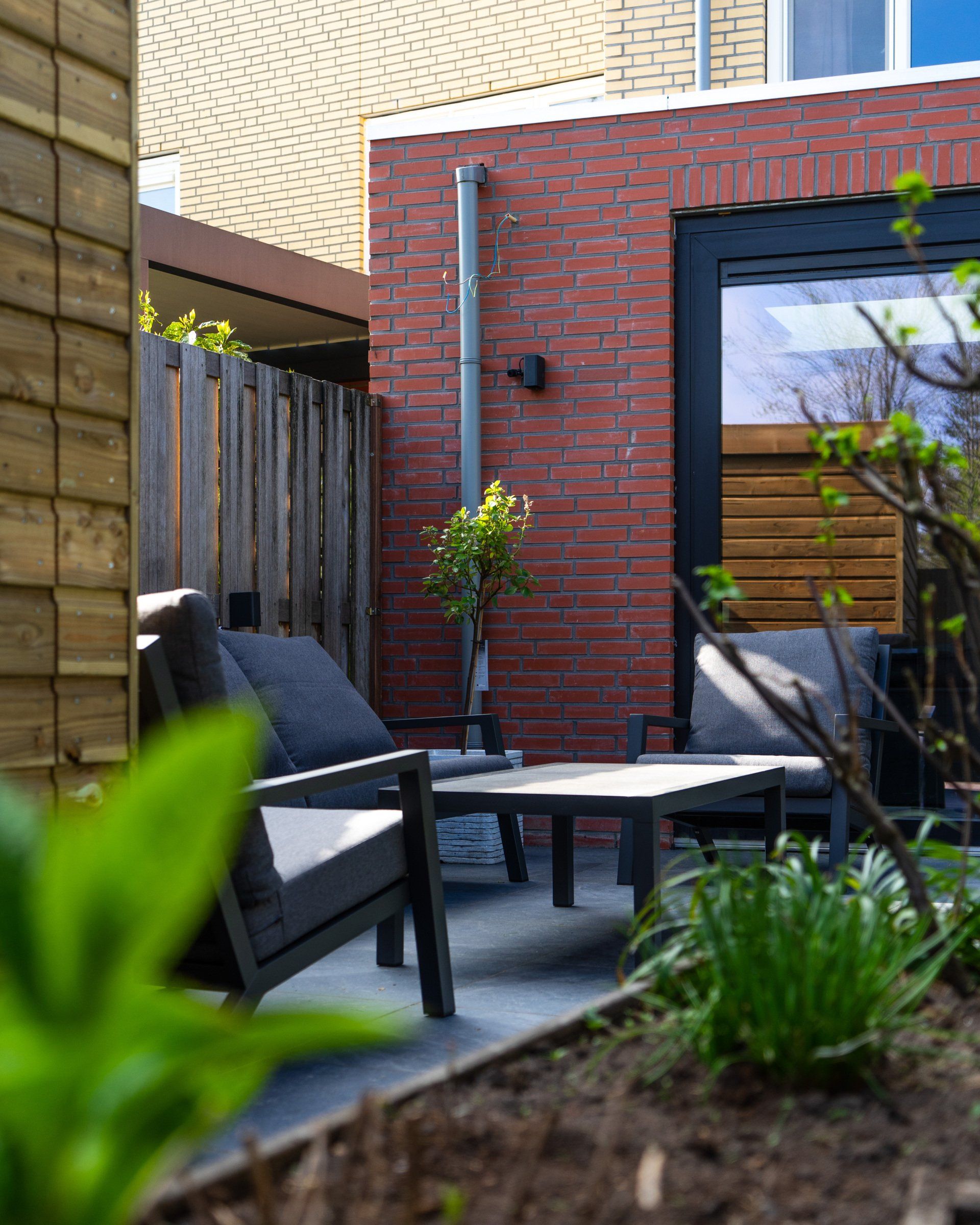 Buitenpatio met zwart meubilair, een rode bakstenen muur en weelderig groen.