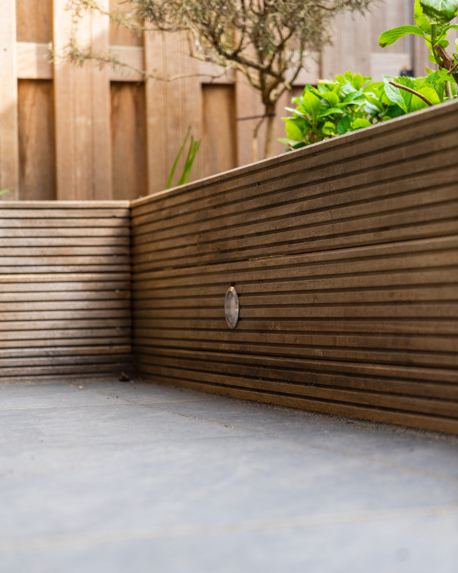 Houten keermuur in een tuin met betonnen ondergrond, zonlicht.
