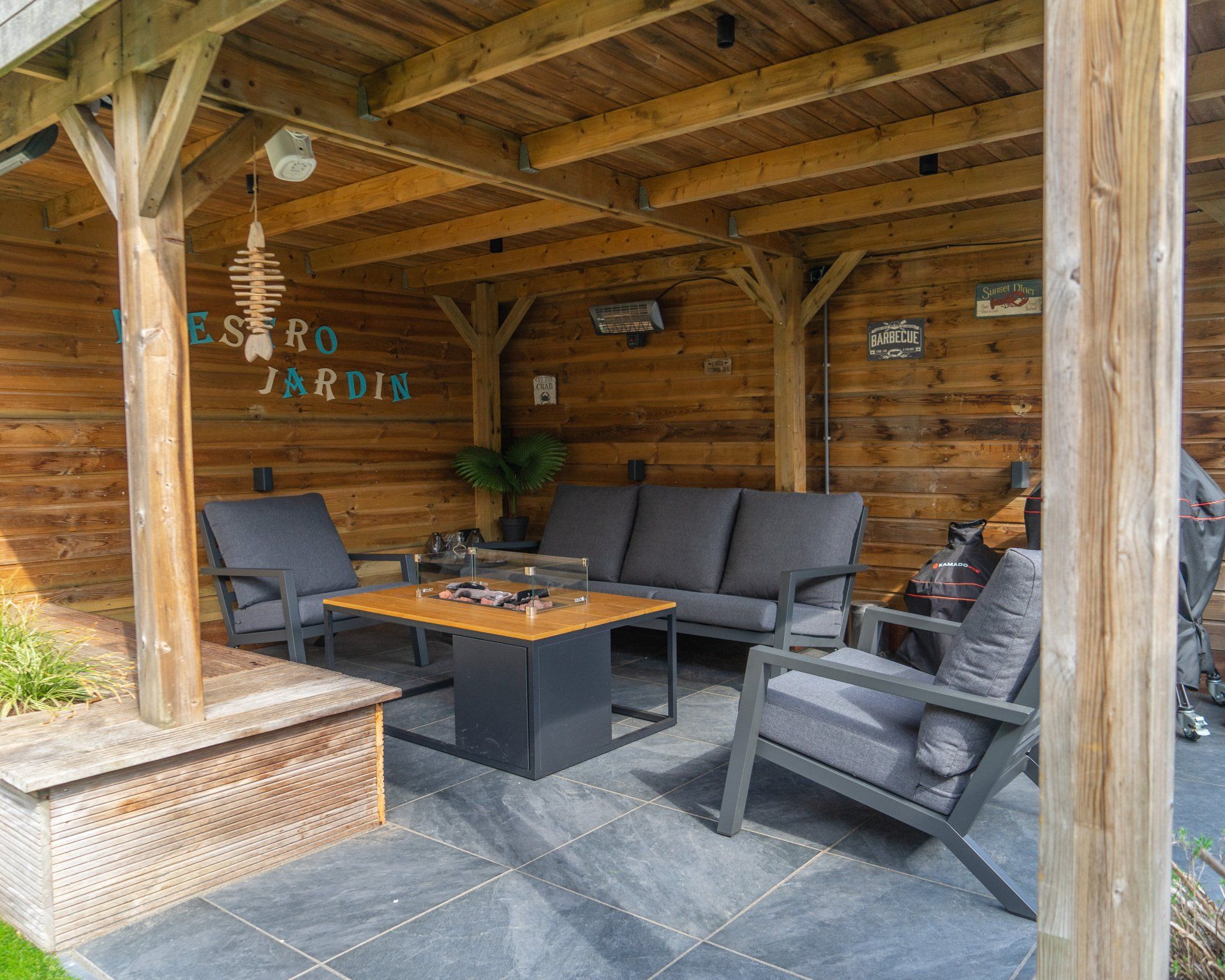 Overdekt terras met tuinmeubilair, een vuurplaats en houten balken.