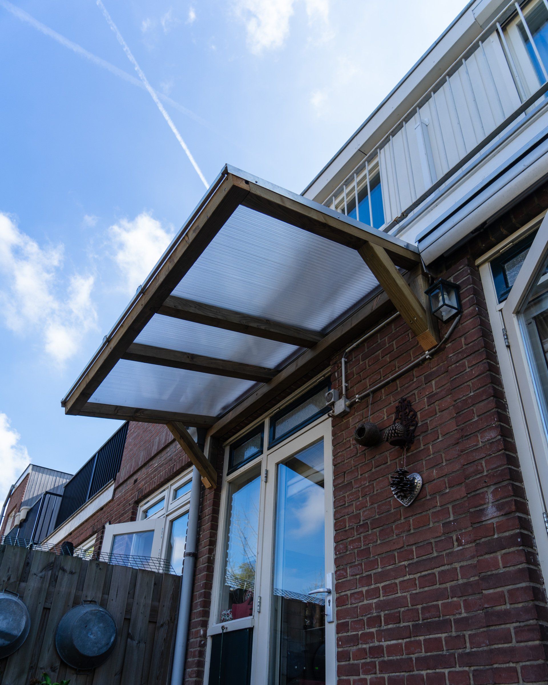 Een houten luifel boven de glazen deuren van een bakstenen gebouw op een zonnige dag.