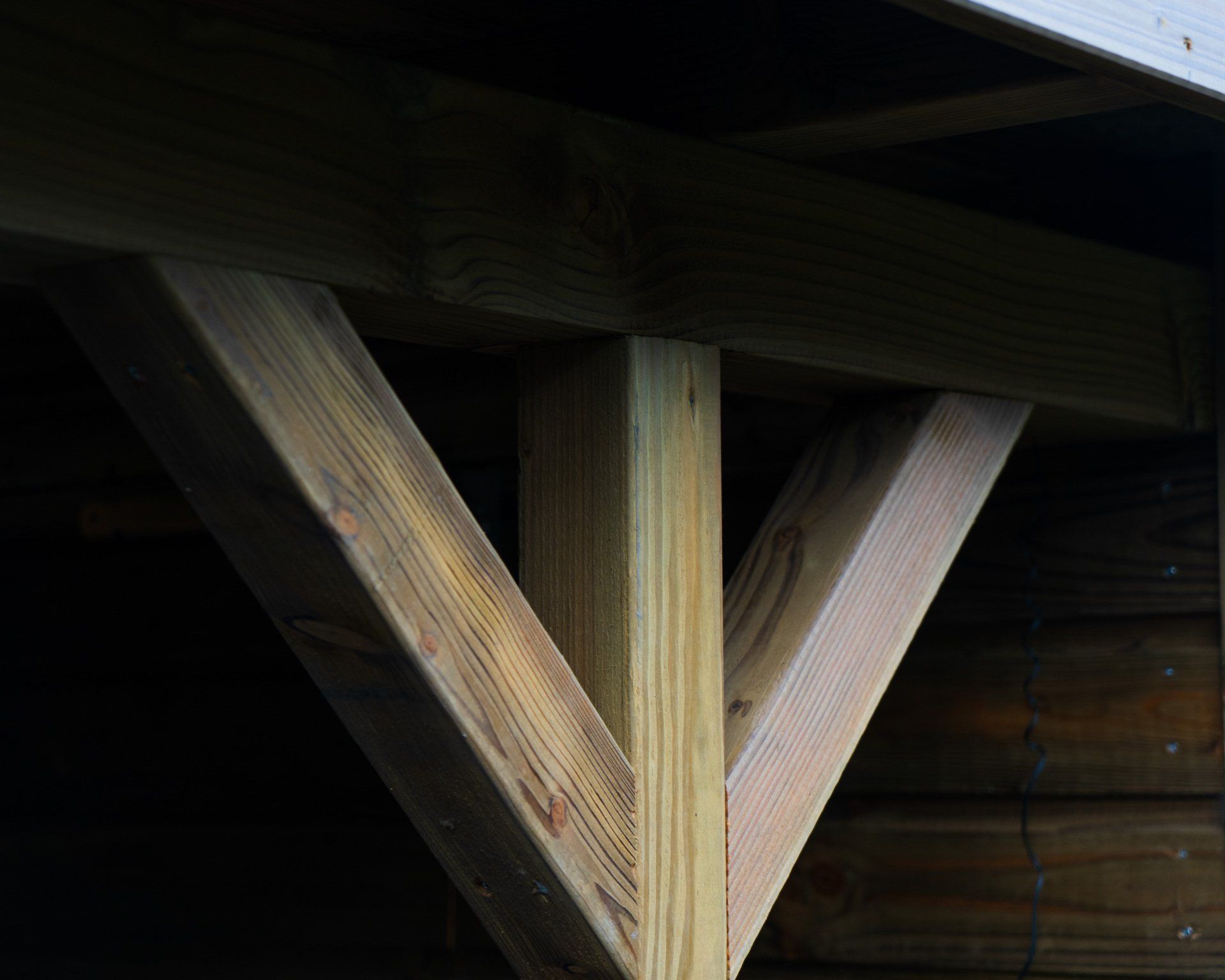 Houten balken ondersteunen het dak van een constructie. Twee schuine balken komen samen in een verticale paal en vormen zo een 