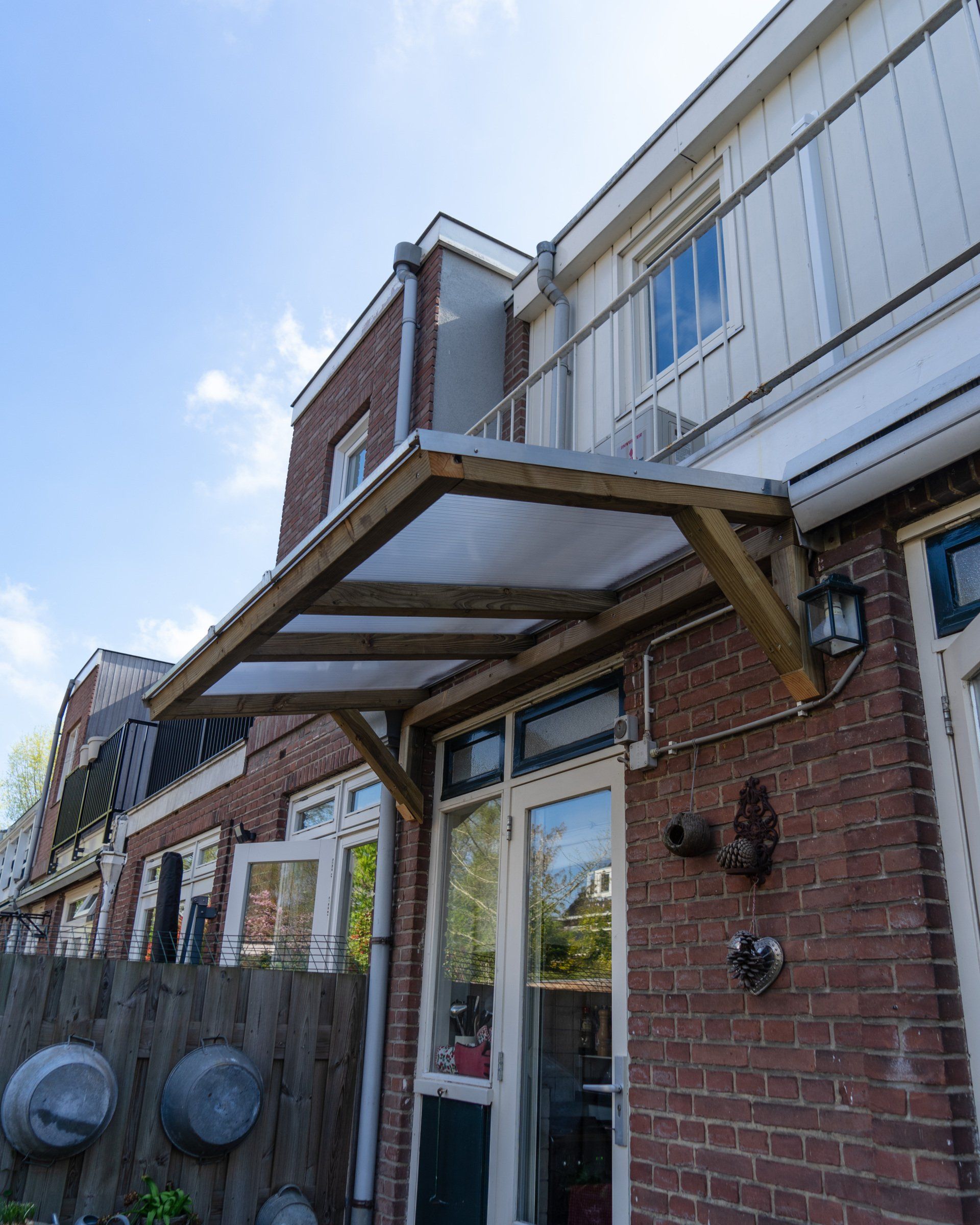 Een houten luifel boven een glazen deur van een bakstenen gebouw, op een zonnige dag.
