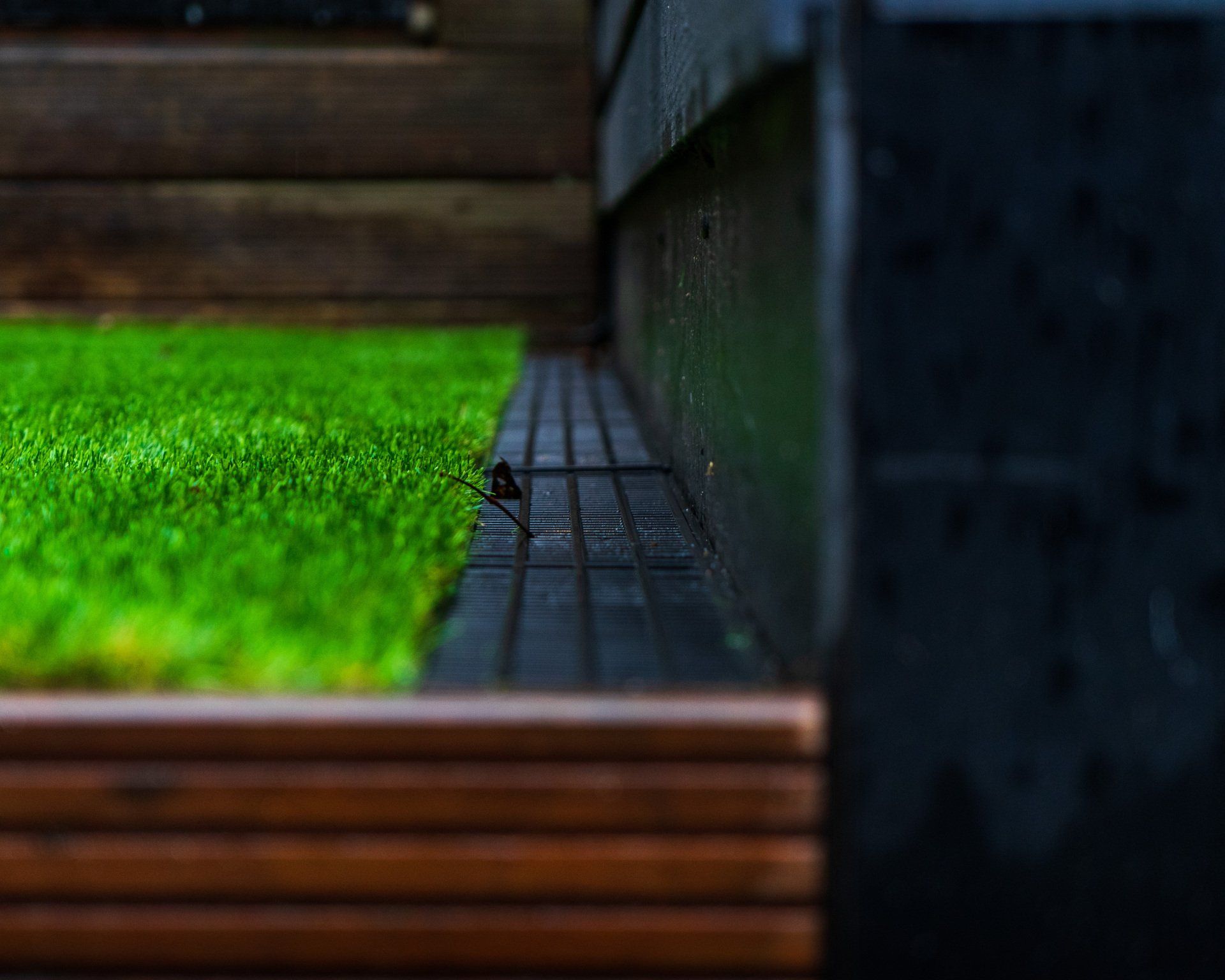 Groen kunstgras naast een houten terras en een zwarte muur, waarmee een kleine buitenruimte wordt afgebakend.