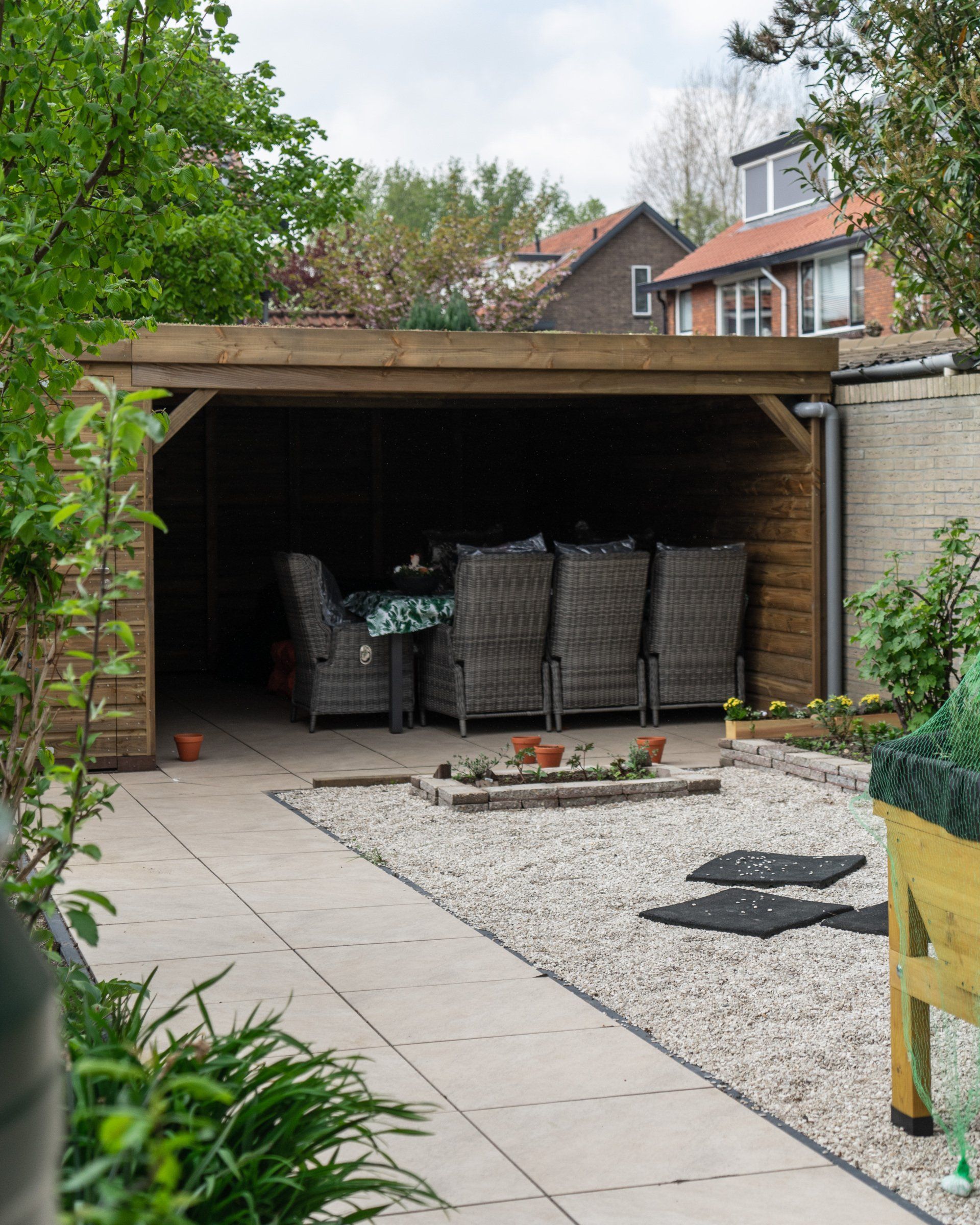 Terras in de achtertuin met een grindpad dat leidt naar een overdekte eethoek met tafel en stoelen.