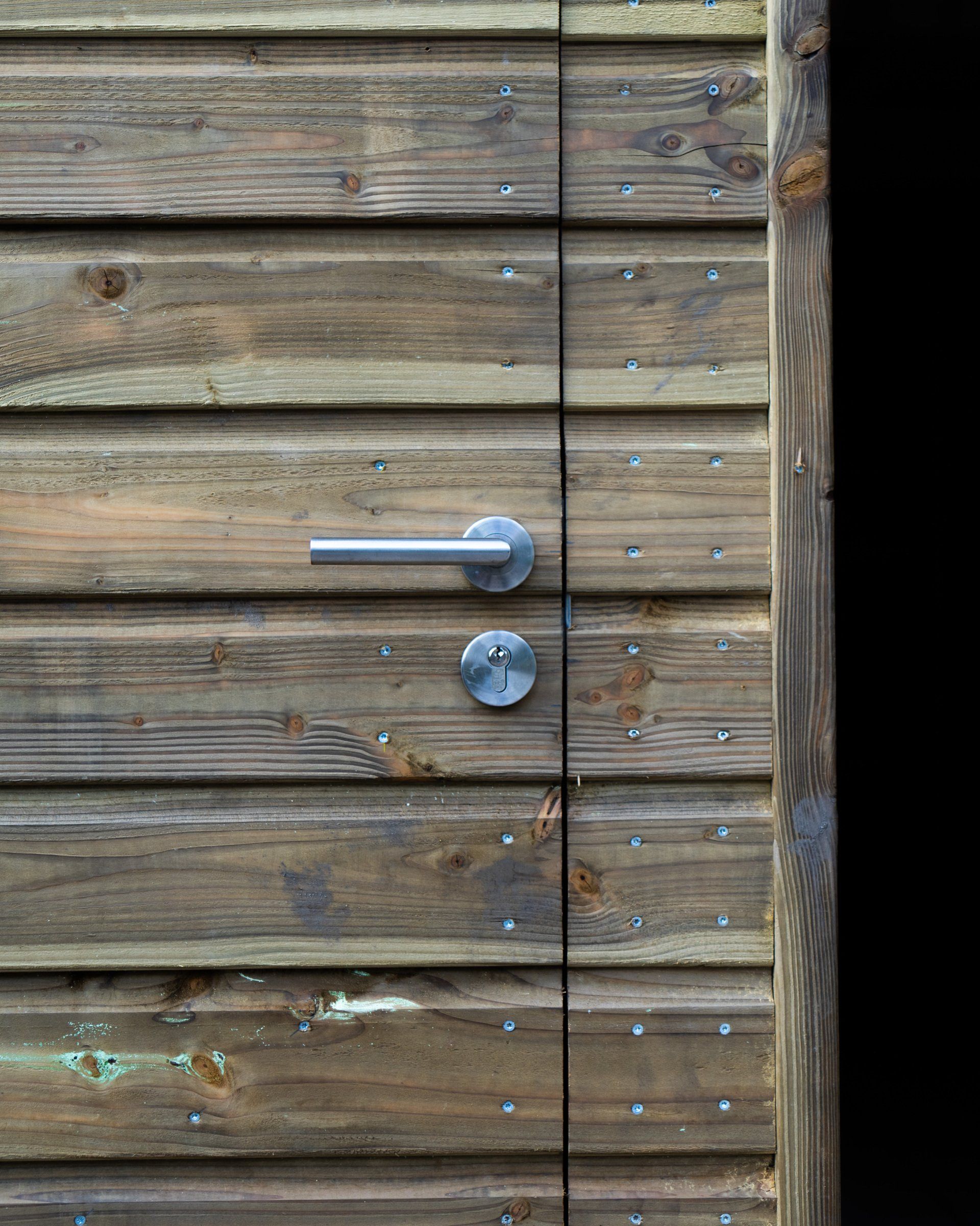 Houten buitendeur met zilverkleurige handgreep en slot.