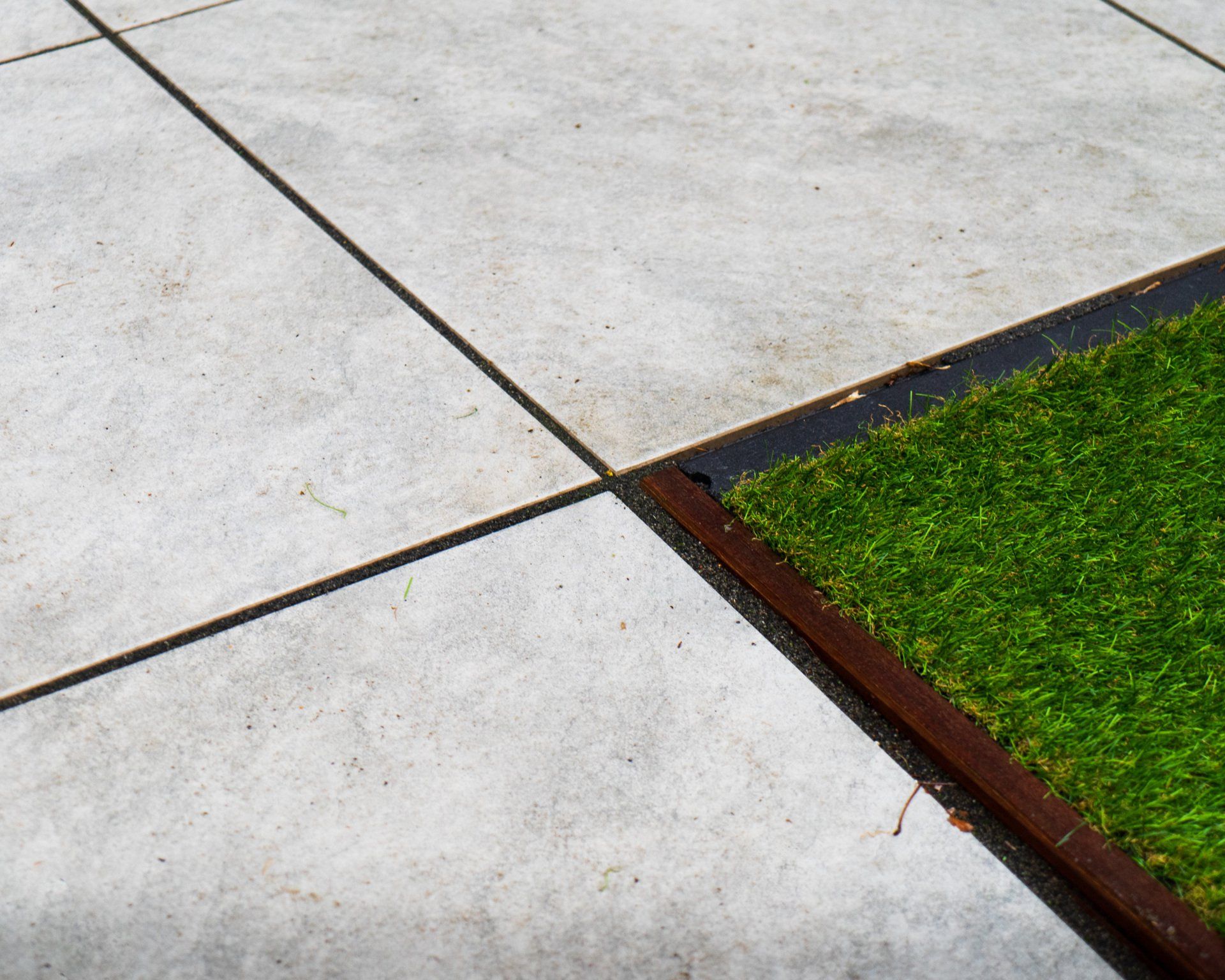 Een betonnen terras met donkere lijnen die een stukje groen gras omringen.