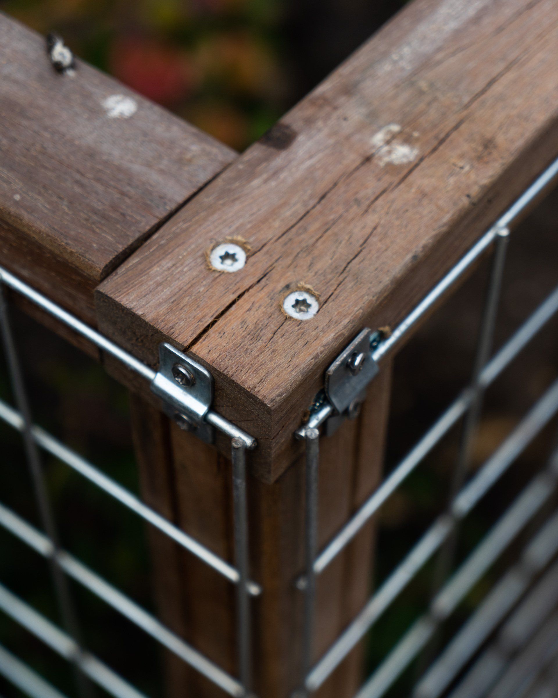 Houten hoekstuk van een terrasreling met metalen draden en bevestigingsmaterialen, buiten.