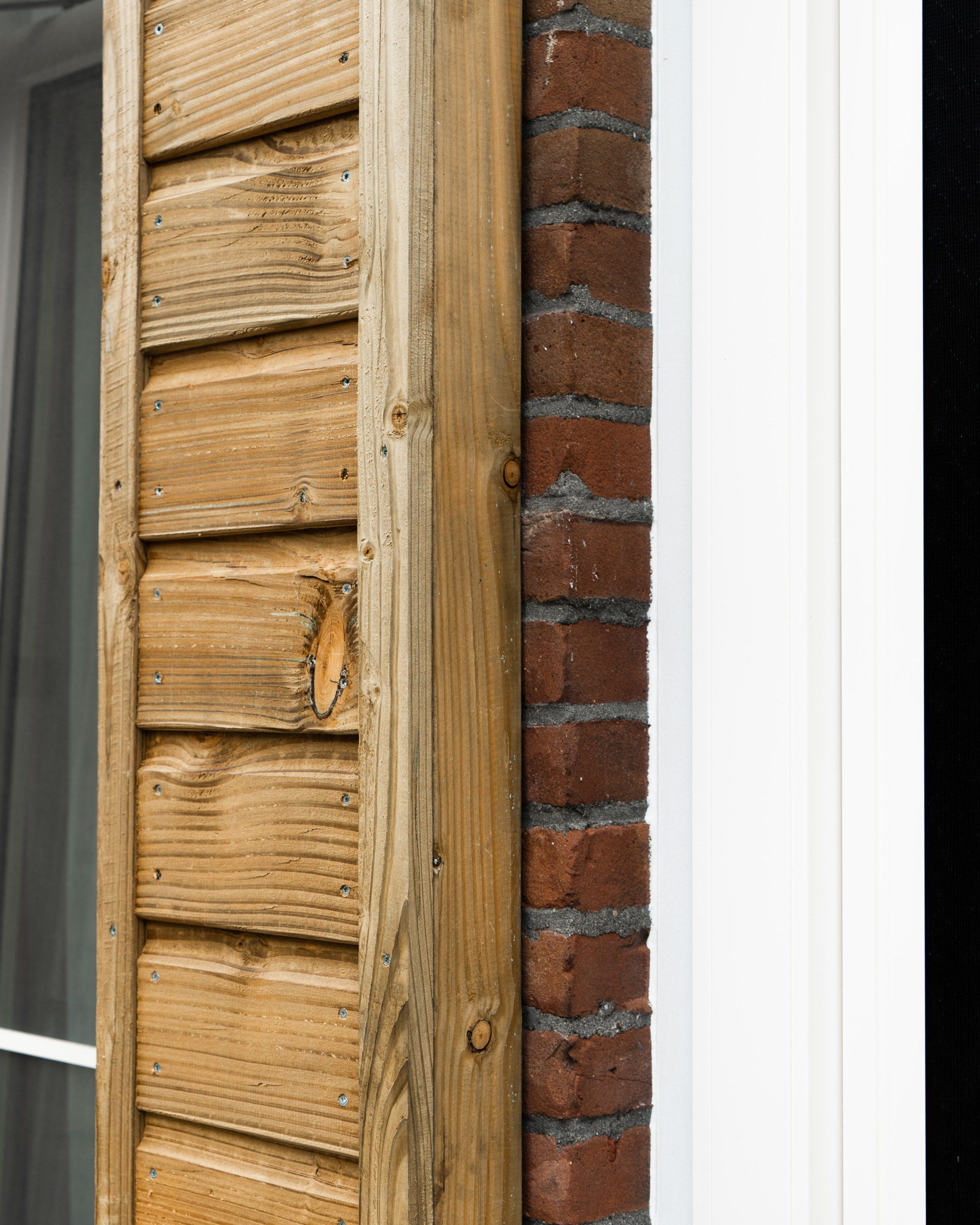 De houten gevelbekleding en de bakstenen buitenmuur komen samen naast een wit deurkozijn.
