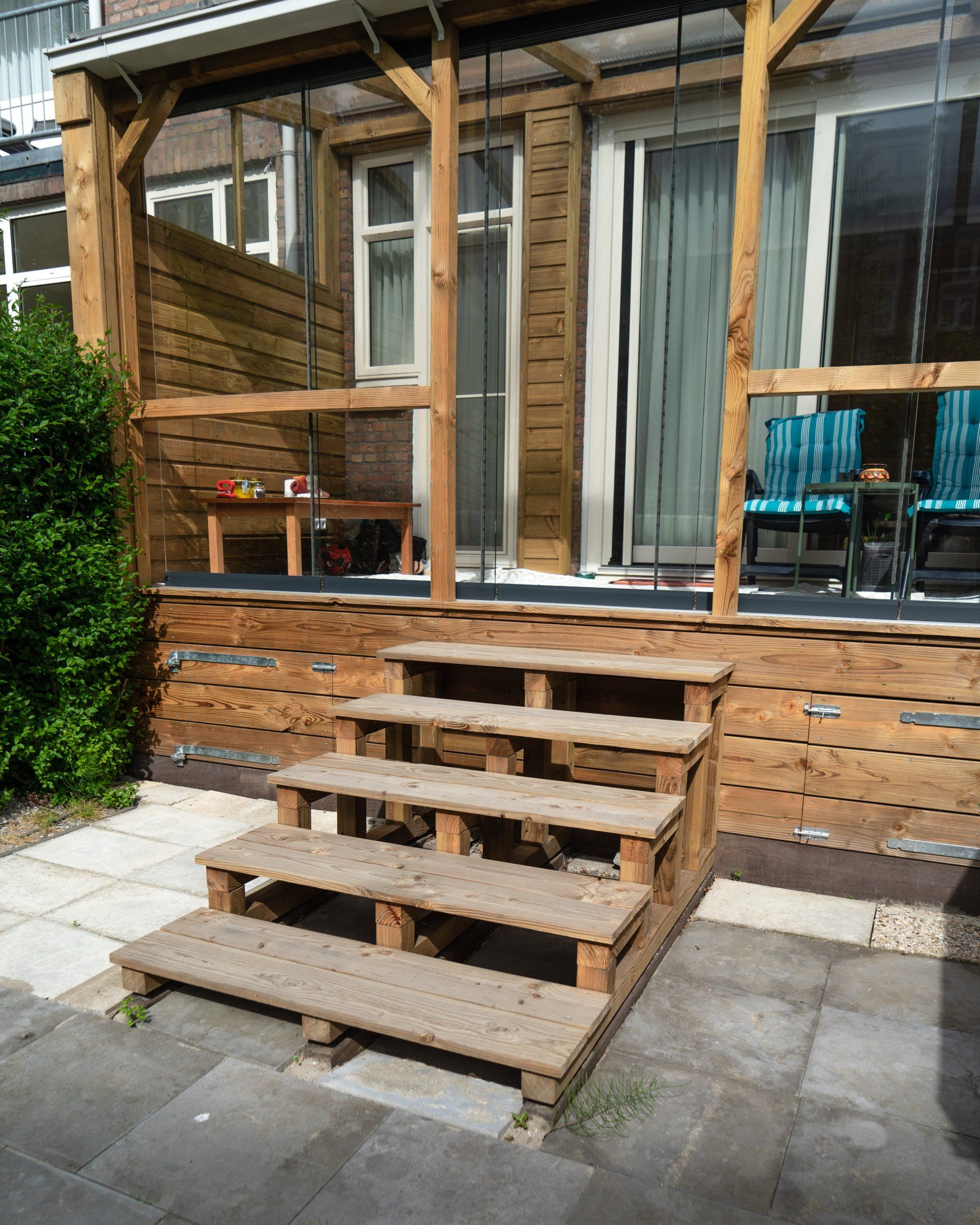 Houten trap naar een terras met een tafel en stoelen. Zonnige dag, buitenomgeving.