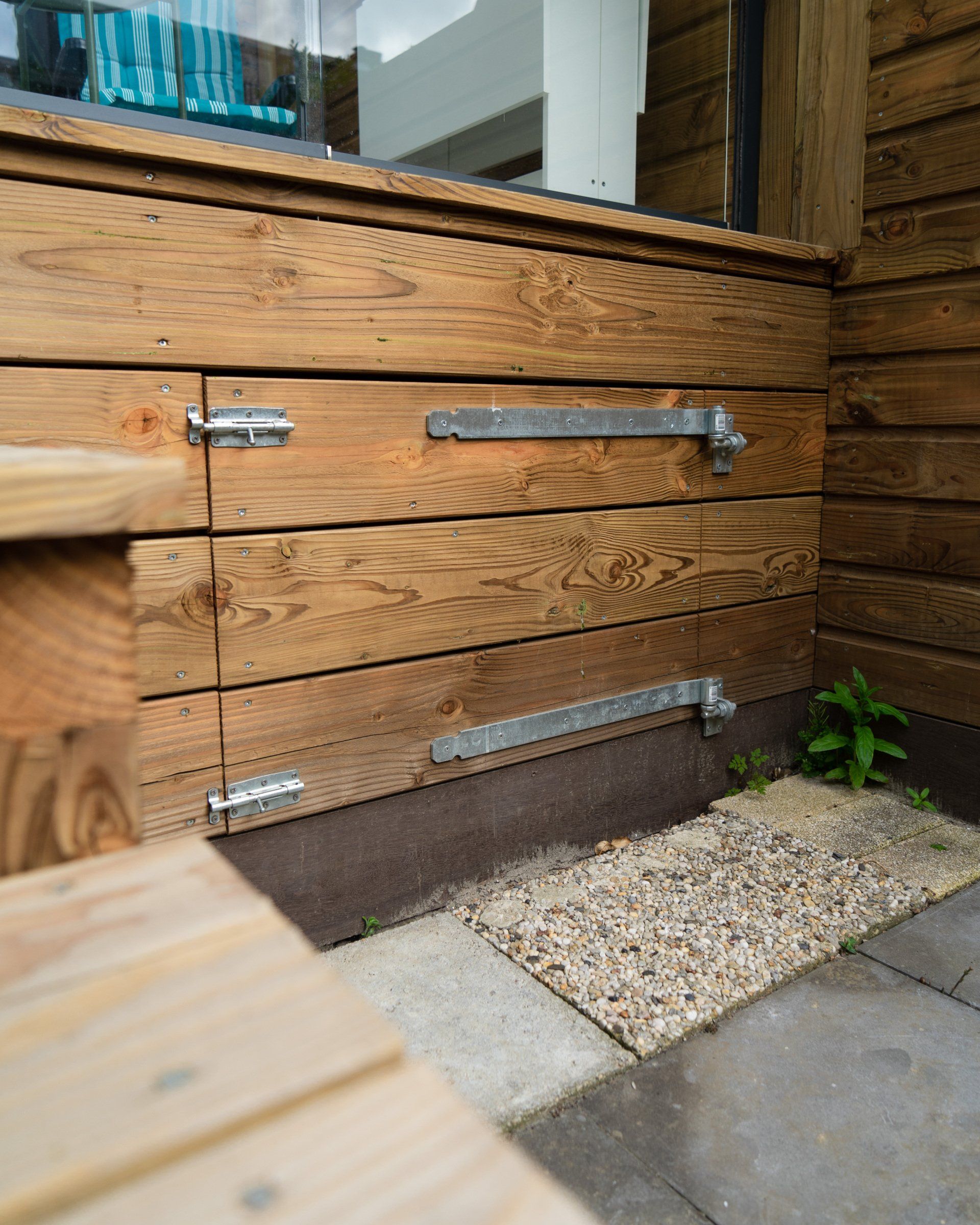 Houten opbergdozen met metalen scharnieren, naast een stenen pad en een klein plantje.