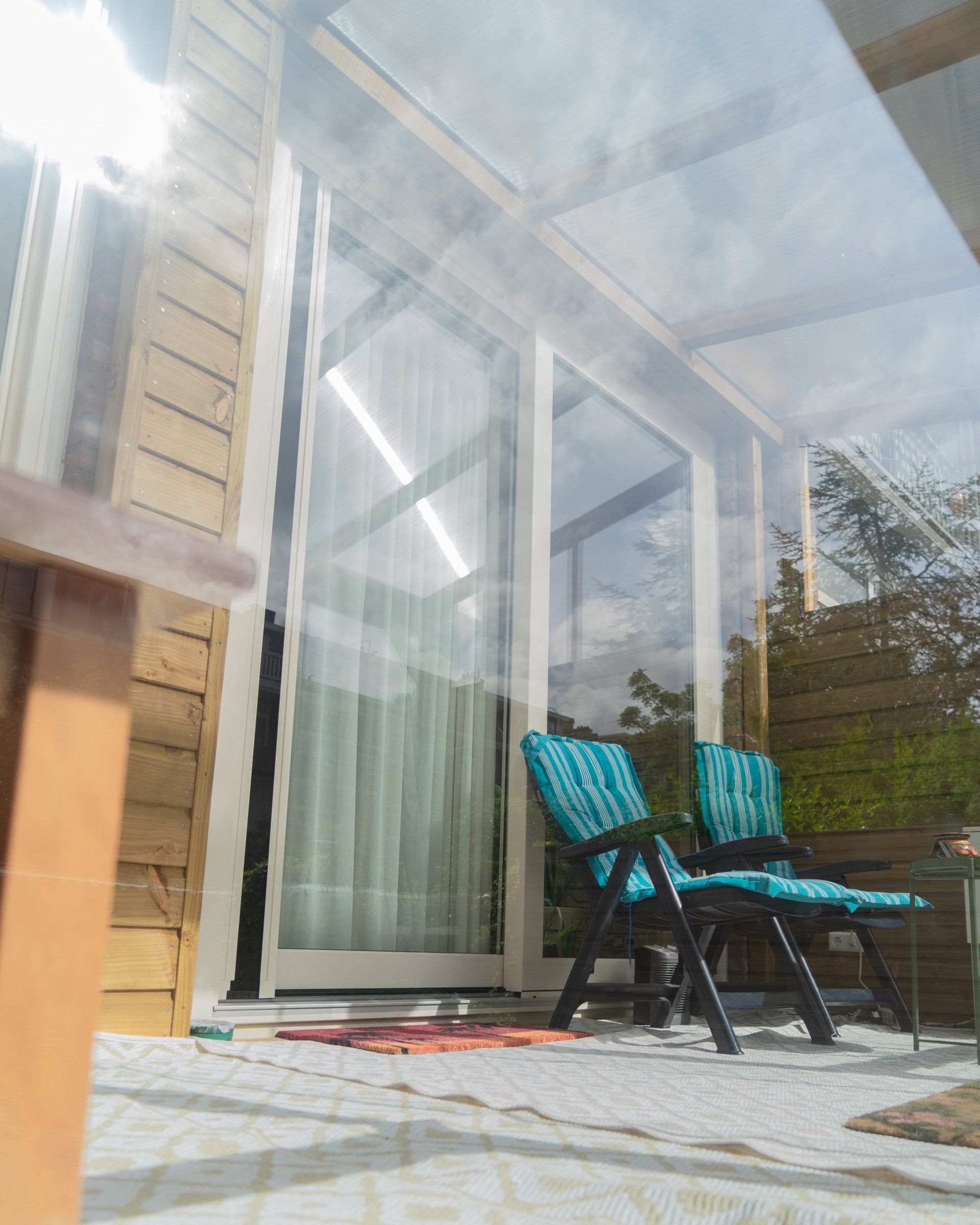 Twee blauwe stoelen op een terras, zonlicht dat weerkaatst op een glazen afscheiding.