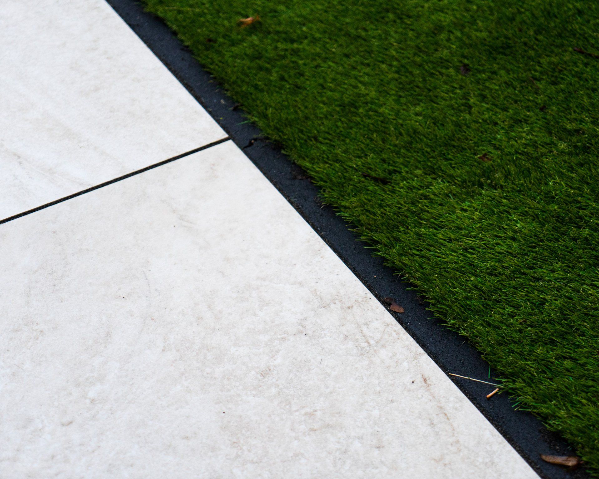 Wit trottoir met een donkere rand, grenzend aan groen kunstgras.