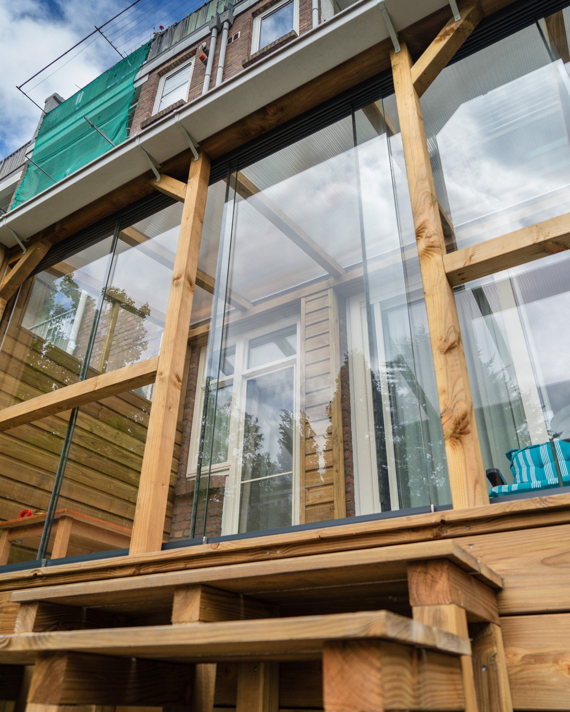 Houten terras met transparante kunststof panelen bevestigd aan de buitenkant van een gebouw.