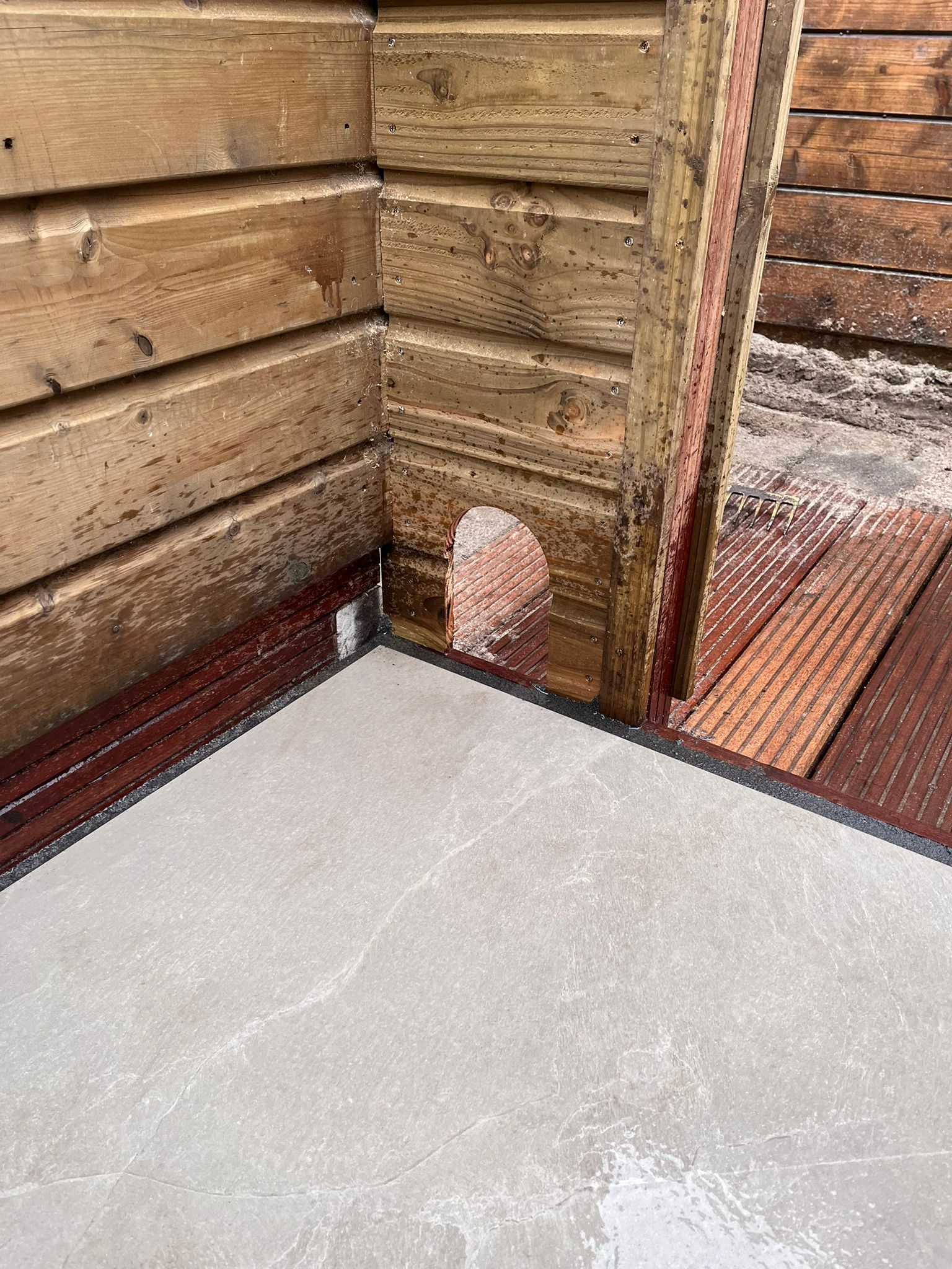 Hoek van een houten schuur met beschadigde planken en een stukje wit materiaal vlakbij de vloer.