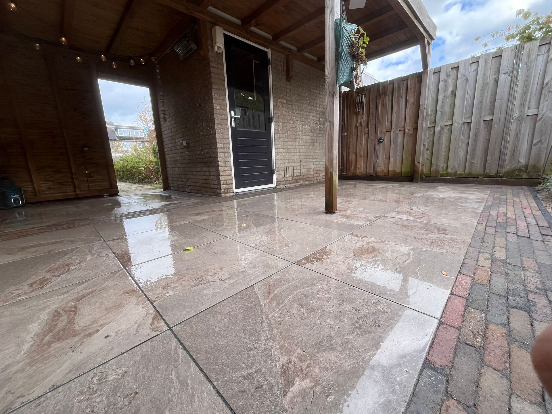 Nat stenen terras met waterplassen. Schuur, houten schutting en bewolkte lucht op de achtergrond.