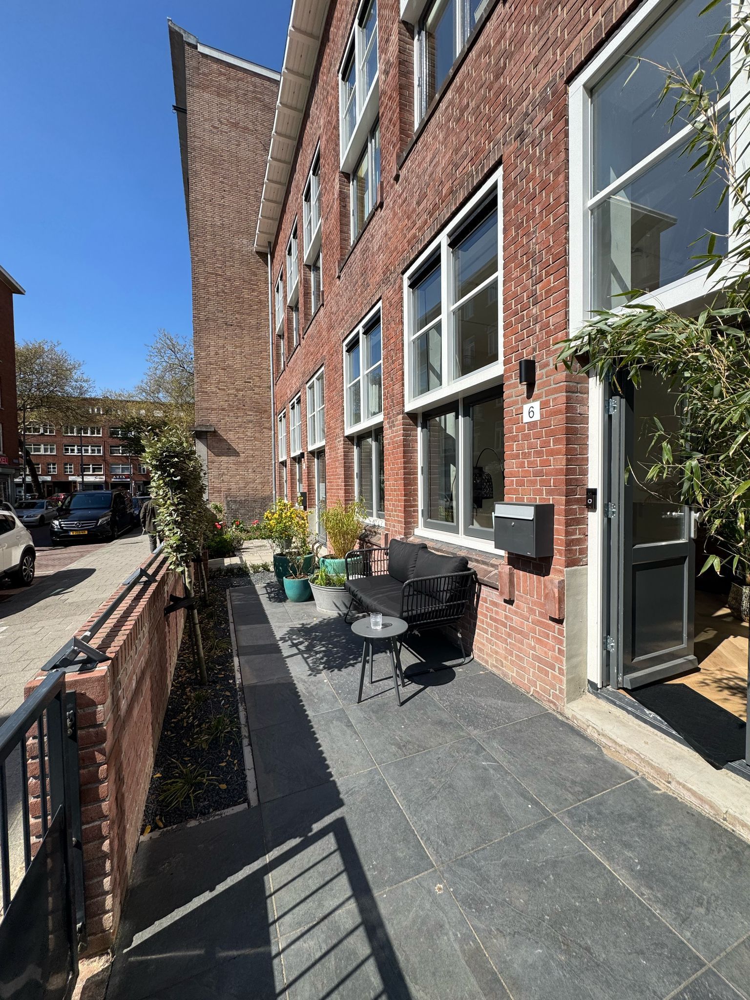 Een bakstenen gebouw met een rij ramen, een klein terras en een barbecue. Een zonnige dag.
