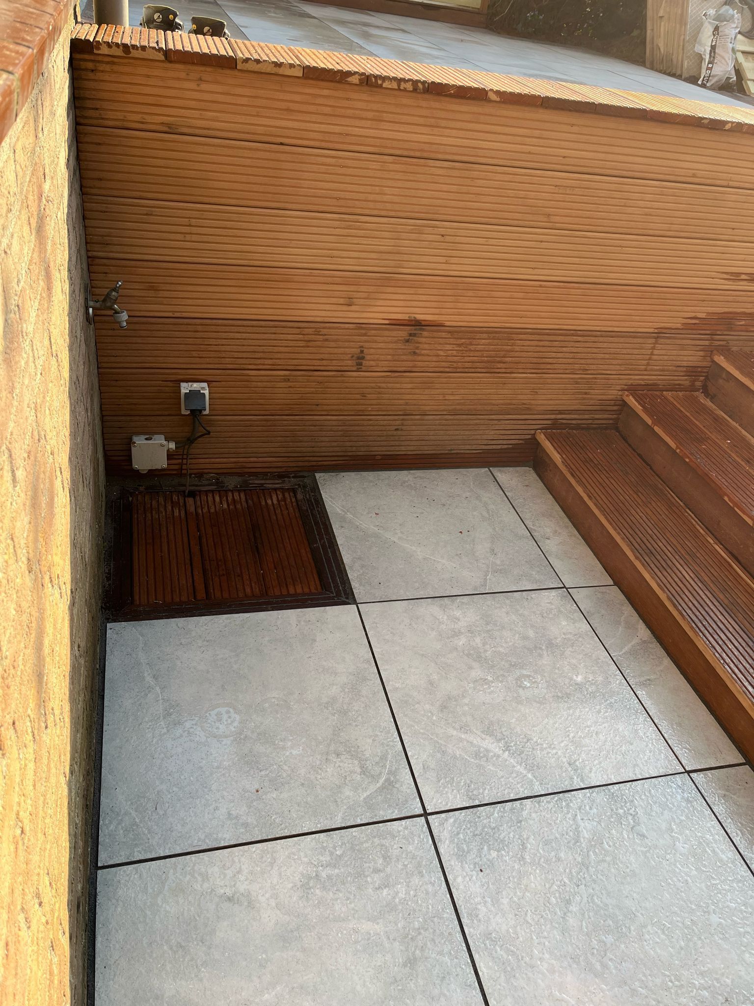 Buitenpatio met houten plafond, betonnen vloer en trappen. Zichtbaar stopcontact.